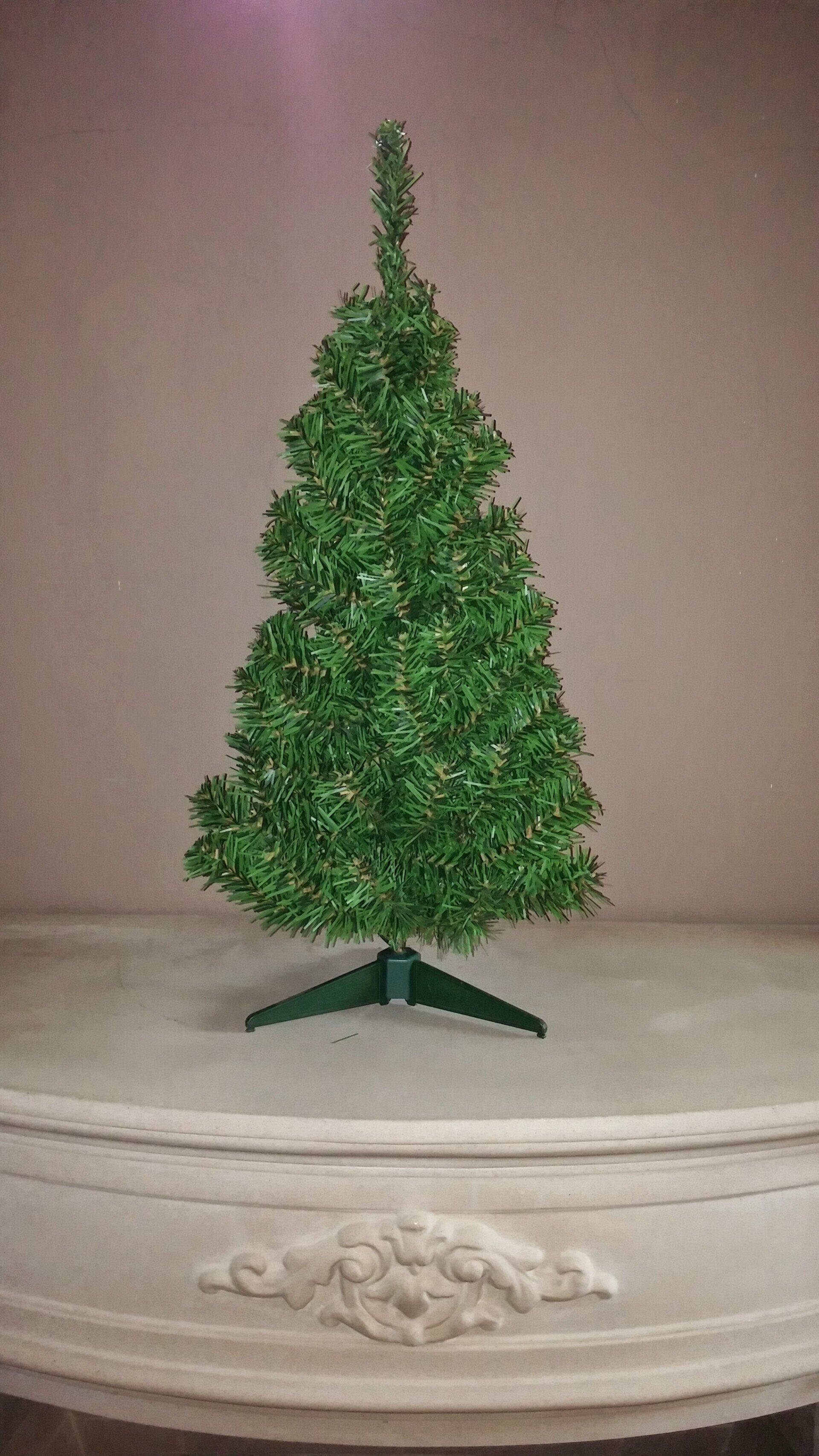 Pequeño árbol de Navidad verde de mesa sobre una superficie decorativa blanca sobre un fondo beige.