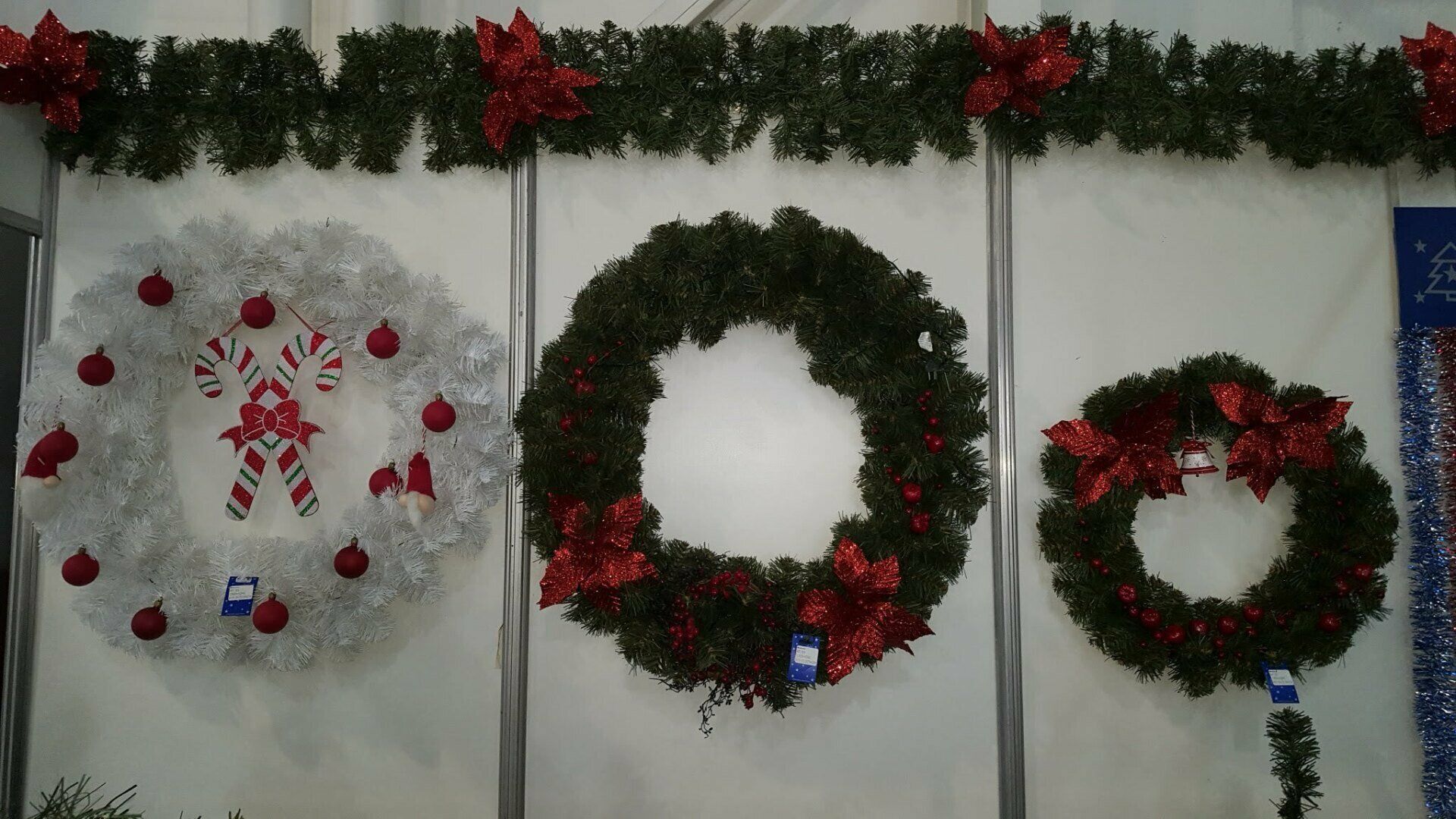 Tres coronas navideñas con adornos rojos y verdes cuelgan de una pared blanca.