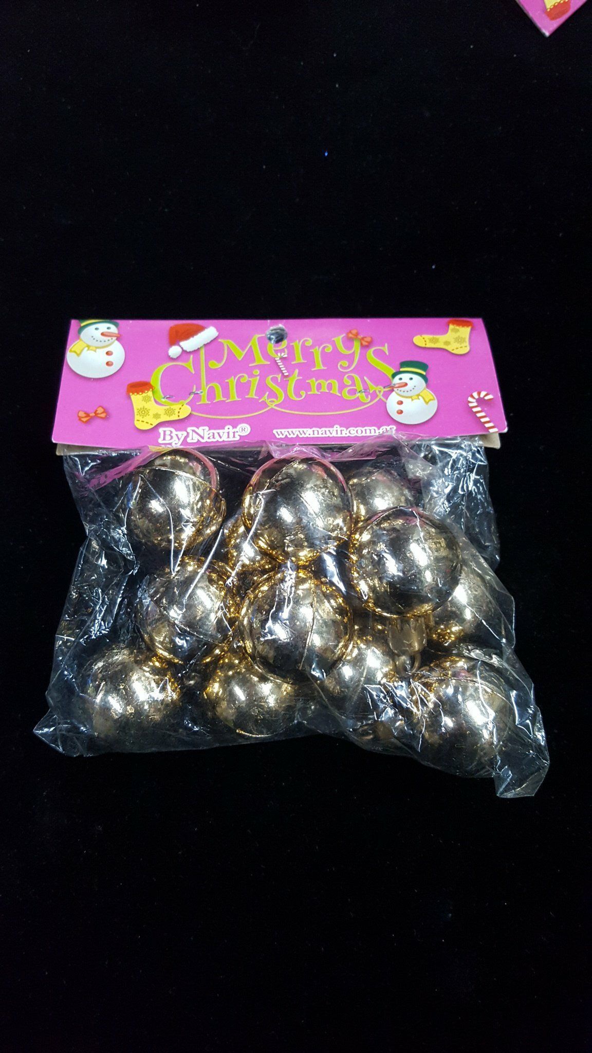 Bolsa de brillantes adornos navideños con una etiqueta rosa de vacaciones sobre fondo oscuro.