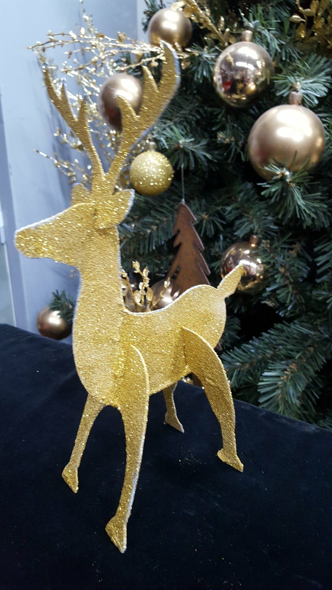 Adorno de reno con purpurina dorada en un árbol de Navidad con bolas doradas.
