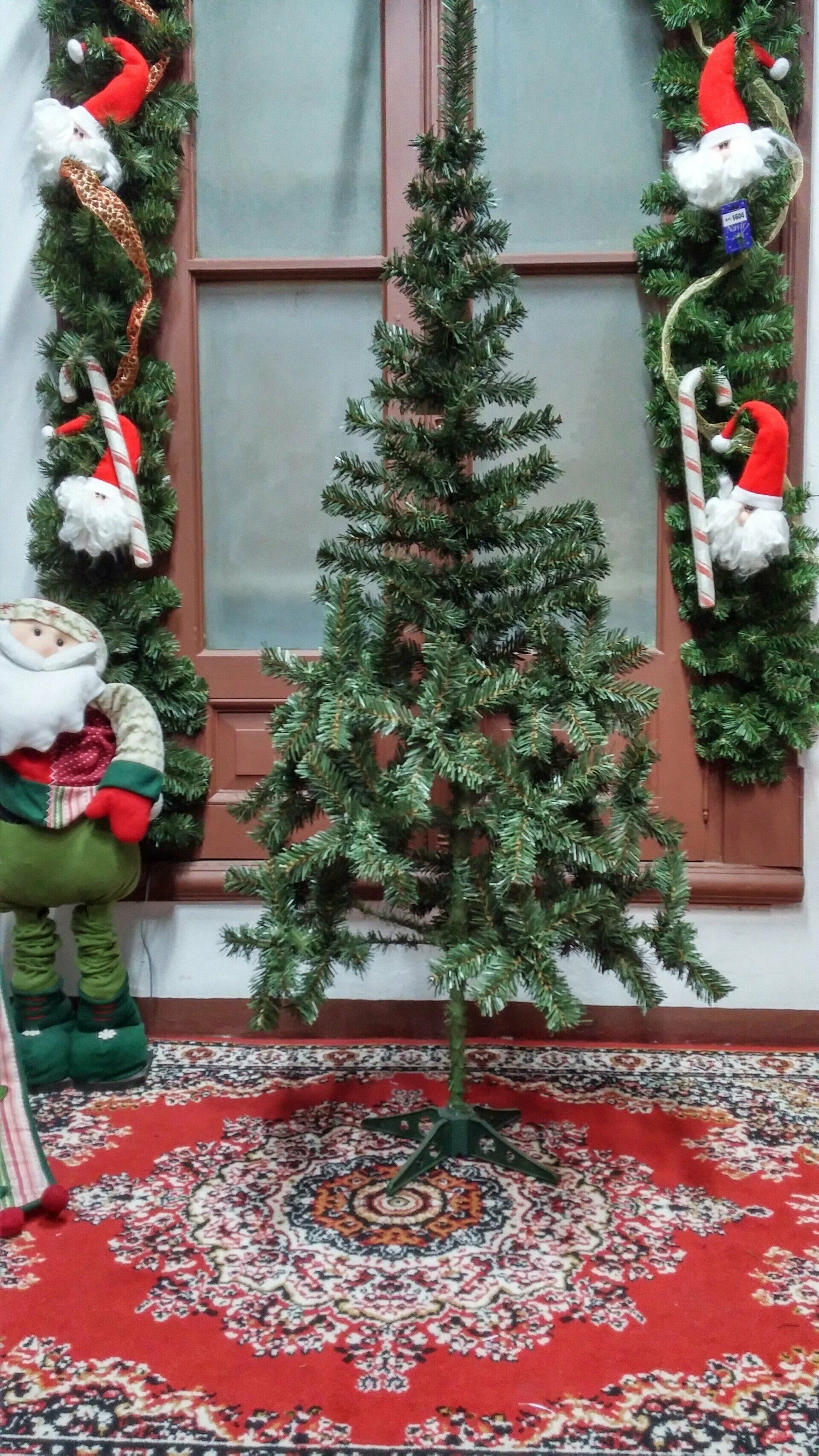 Árbol de Navidad decorado sobre una alfombra roja estampada, enmarcado por guirnaldas navideñas y elfos.