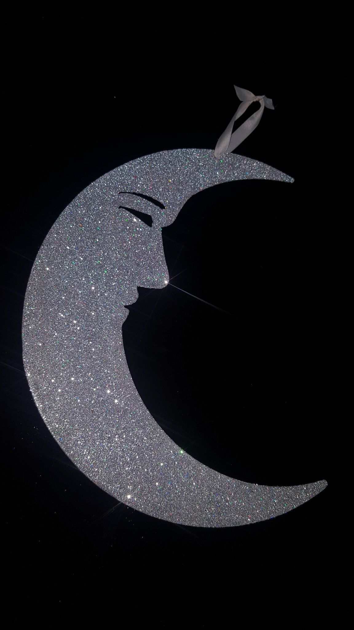 Colgante brillante en forma de media luna con la silueta de un pequeño velero sobre fondo negro.