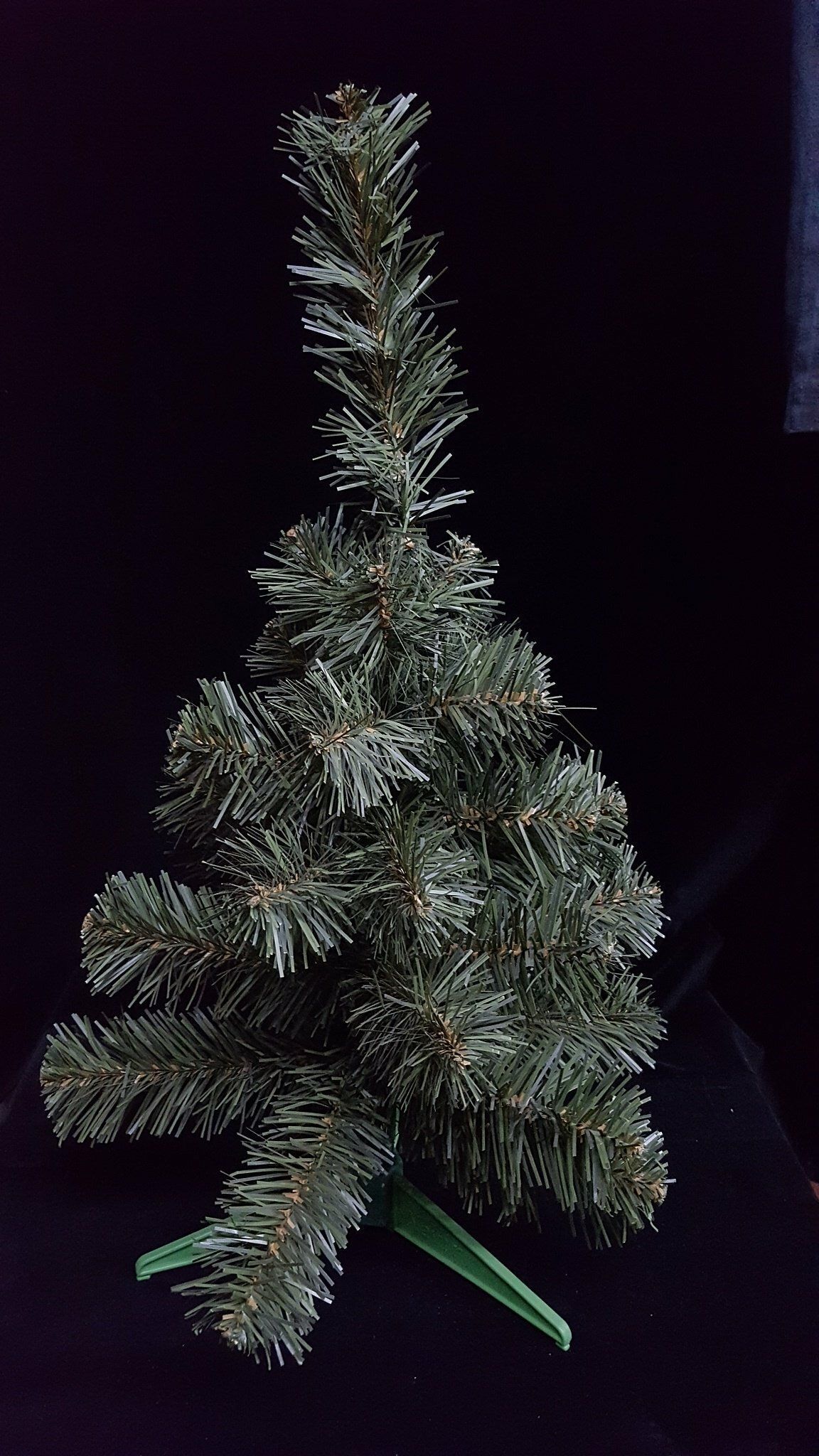Pequeño árbol de Navidad artificial con escasas ramas verdes sobre un fondo oscuro.