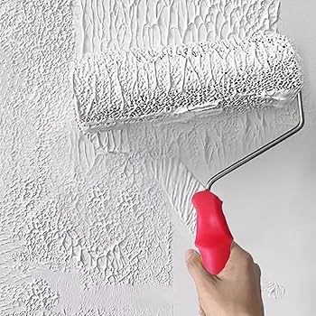 White paint roller on a textured wall, with a red handle held by a hand.
