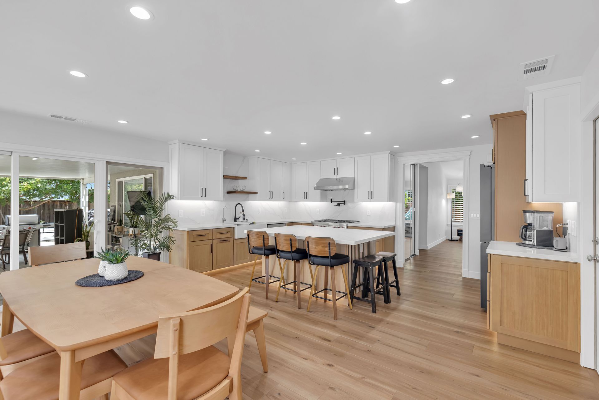 Open-plan kitchen and dining area with light wood floors, white cabinets, and a central island with bar stools.