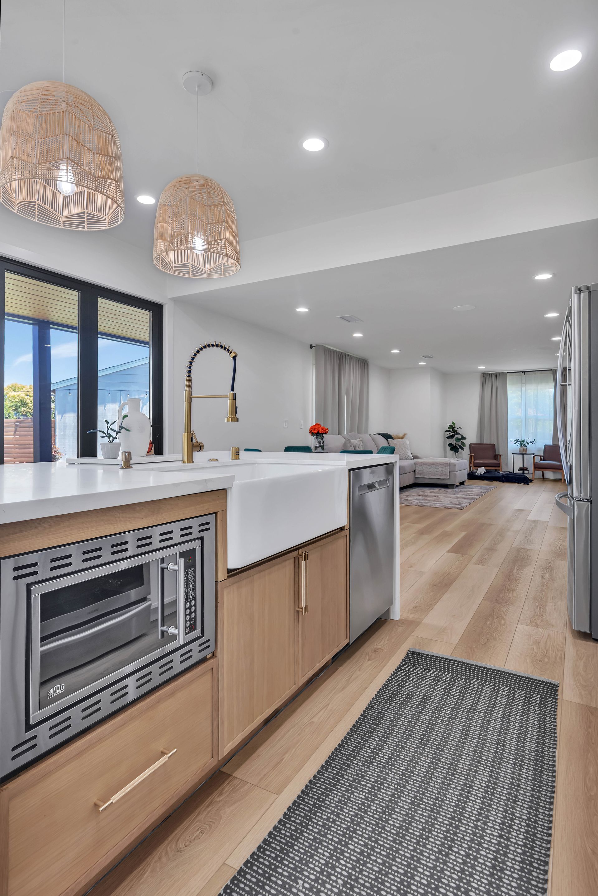 Modern kitchen with wood cabinets, white countertops, and woven pendant lights.