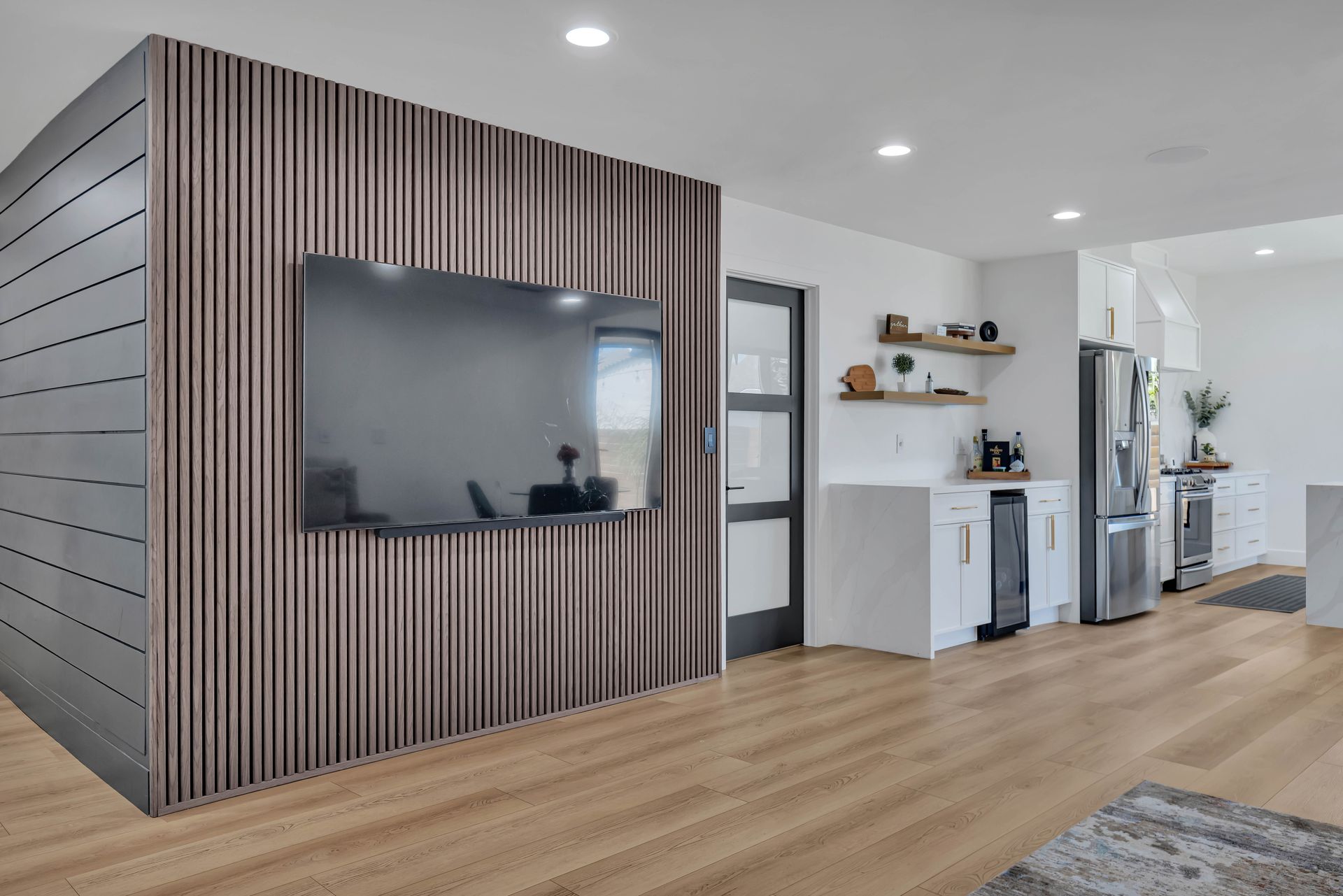 Modern living room with a TV on a wood-paneled wall and light wood flooring.