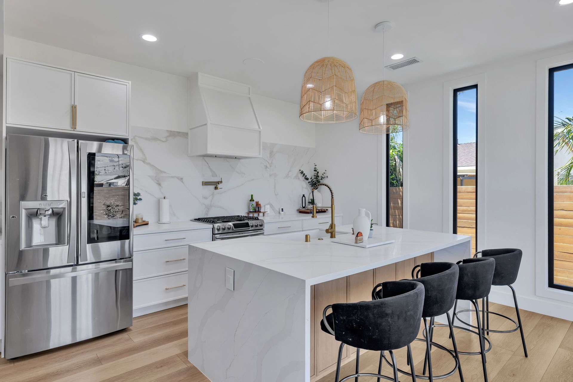 Modern kitchen with light wood cabinetry, white countertops, and two windows.