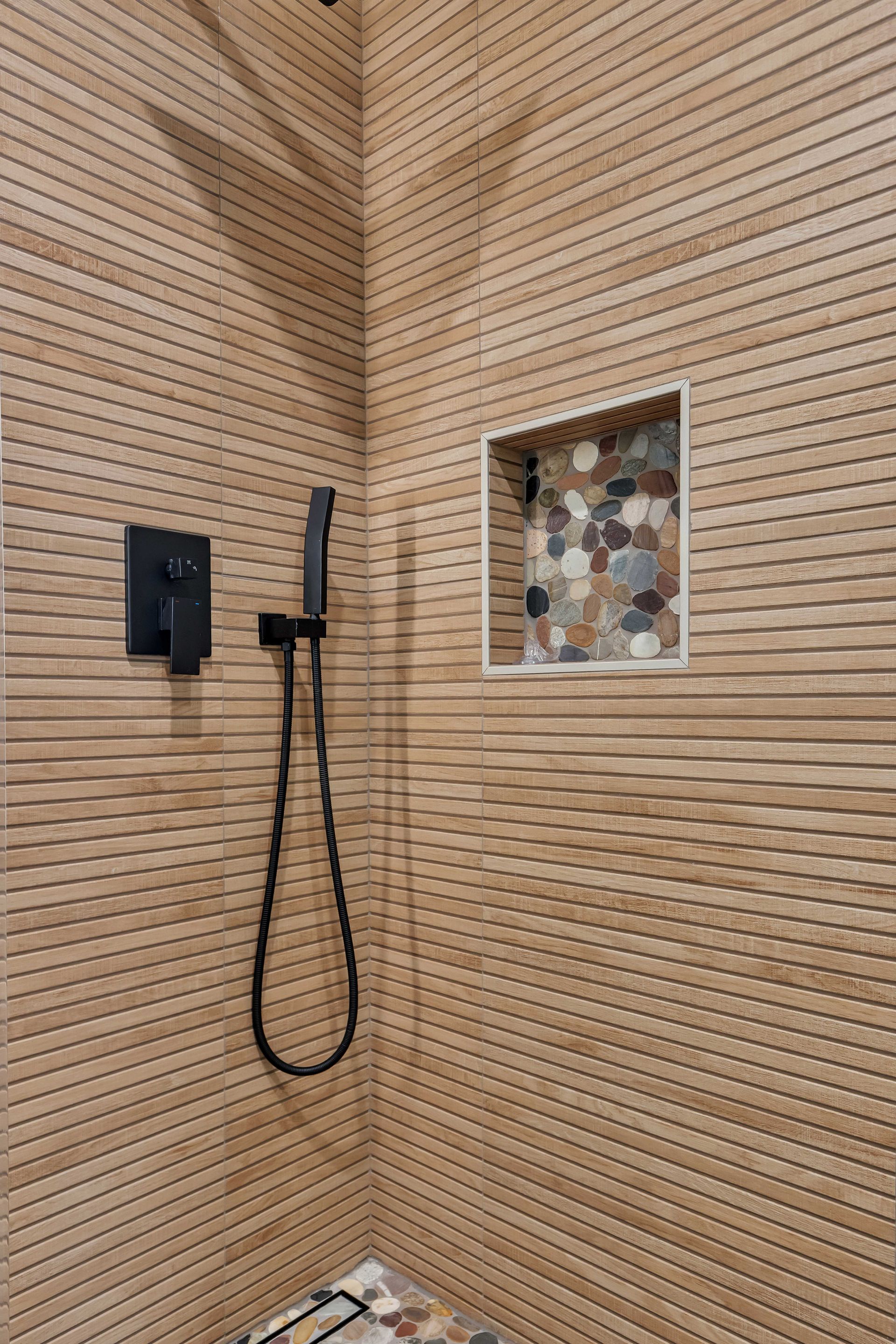 Shower with textured beige tile walls, black fixtures, and a stone-tiled niche.
