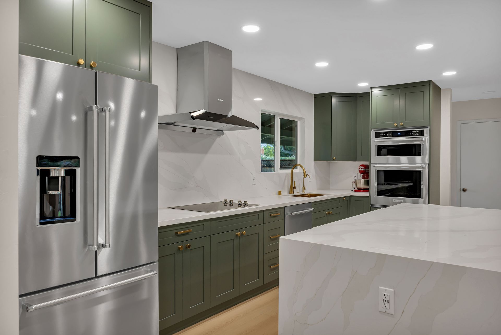 Modern kitchen with green cabinets, stainless steel appliances, and a white countertop island.