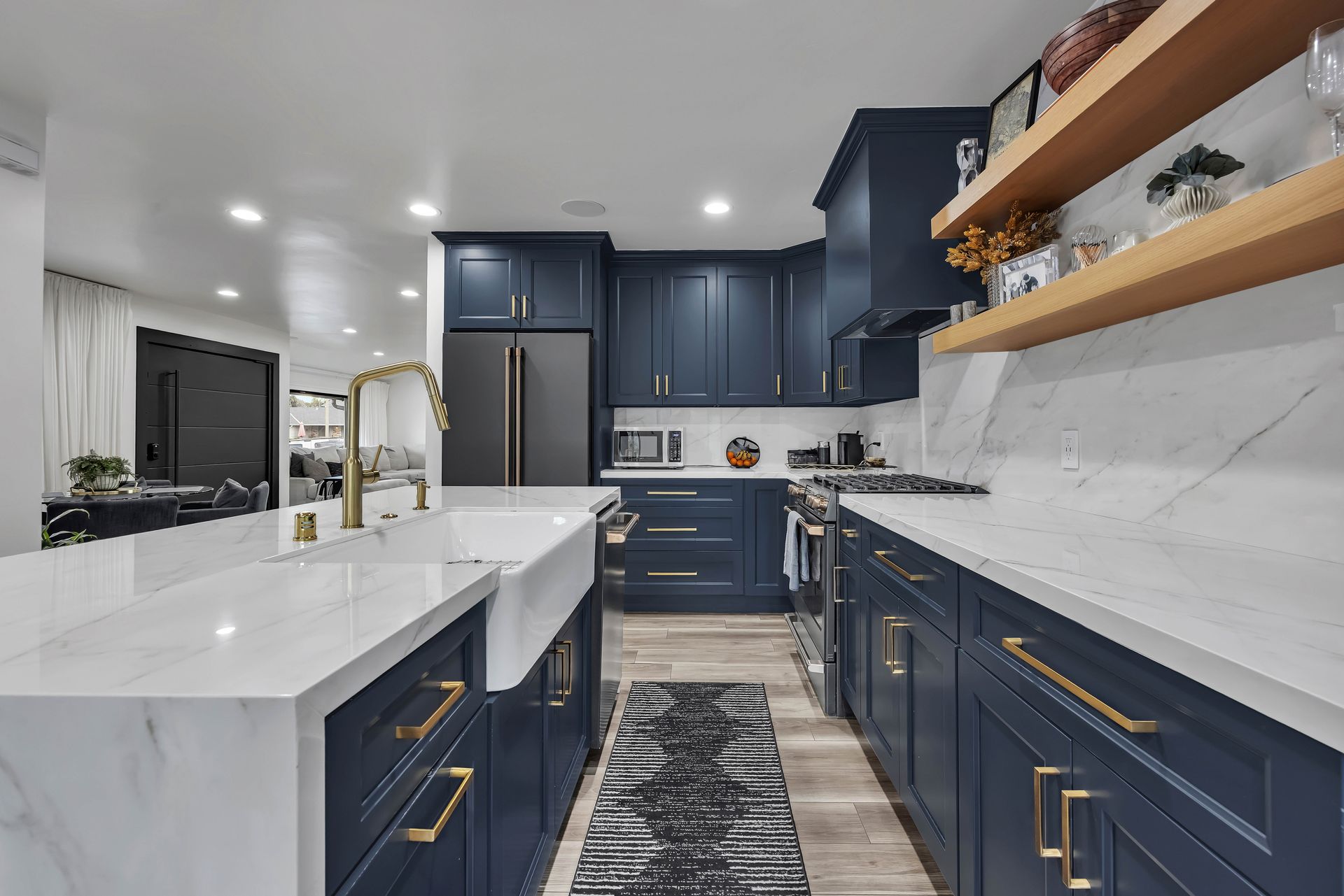 Navy blue kitchen with white countertops and gold hardware. Includes farmhouse sink and wood shelving.