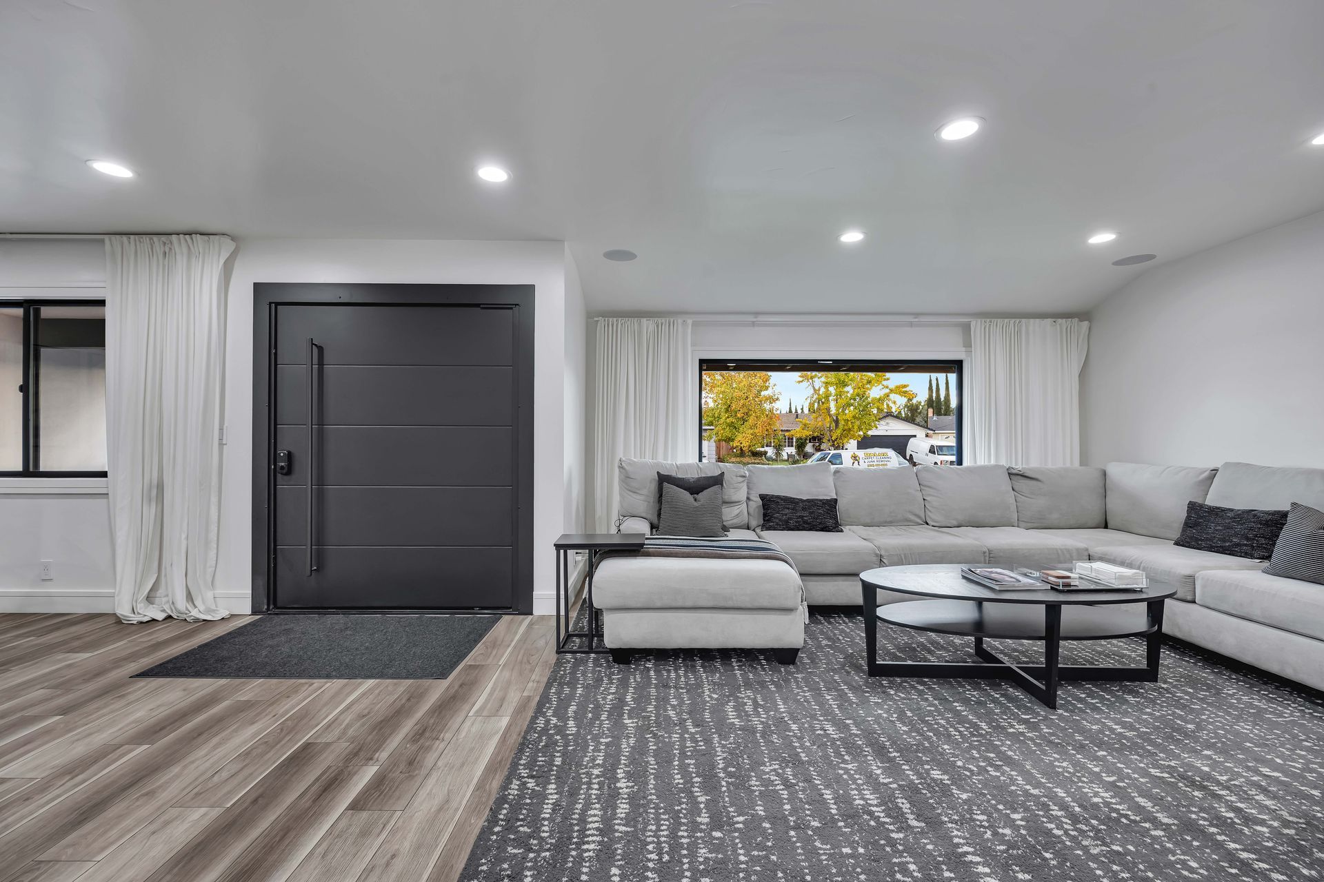 Modern living room with sectional sofa, gray rug, and large window. Dark gray door.