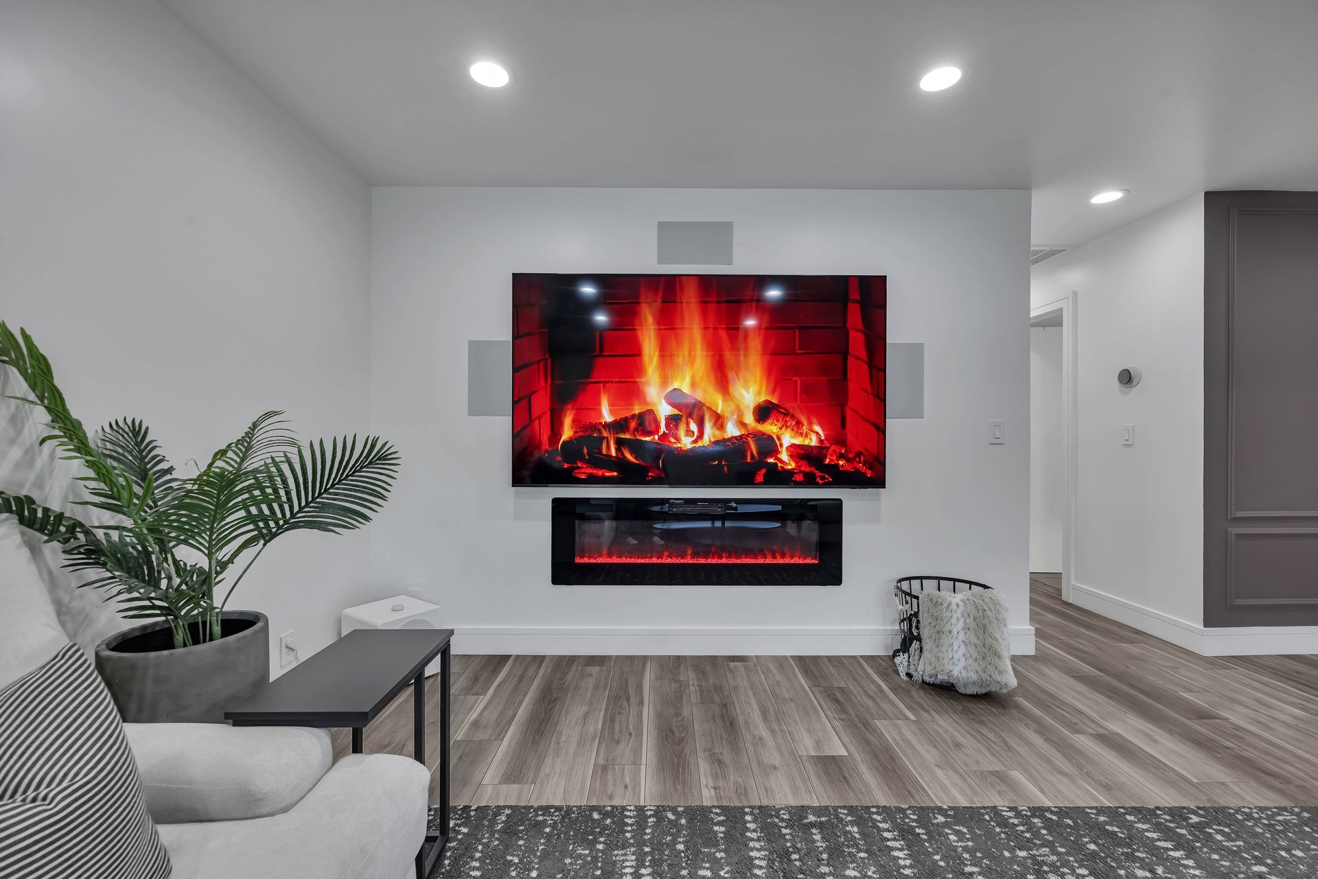 Living room with fireplace and TV mounted on white wall, grey wood floors, potted plant.