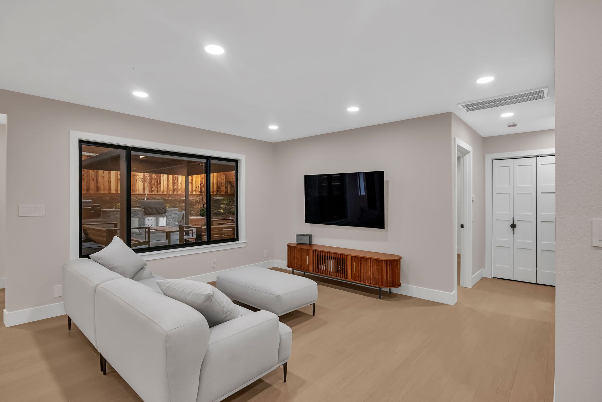 Modern living room with light-colored walls, sofa, TV, wooden console, and window.