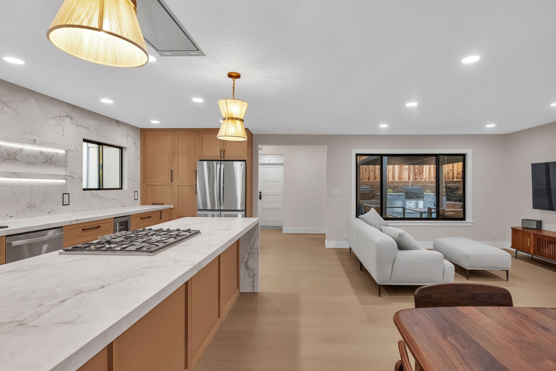 Modern open-concept kitchen and living room with marble countertops, wood cabinets, and a white sofa.