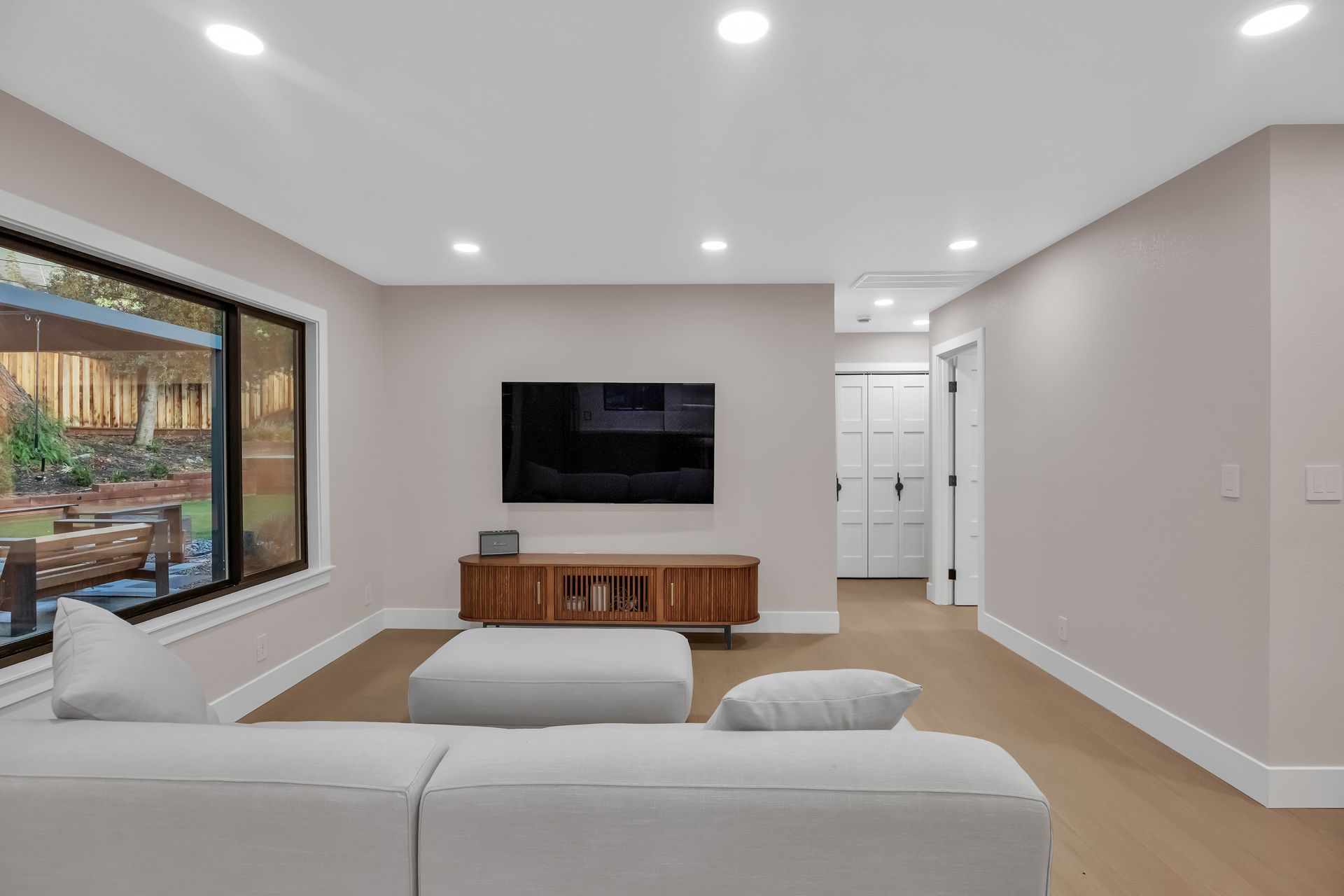 Modern living room with TV, couch, and wooden cabinet, facing a large window.