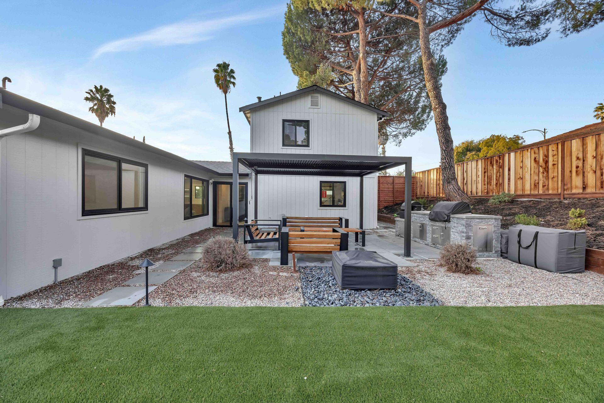 Backyard with a modern white house, patio furniture, a fire pit, and a green lawn.