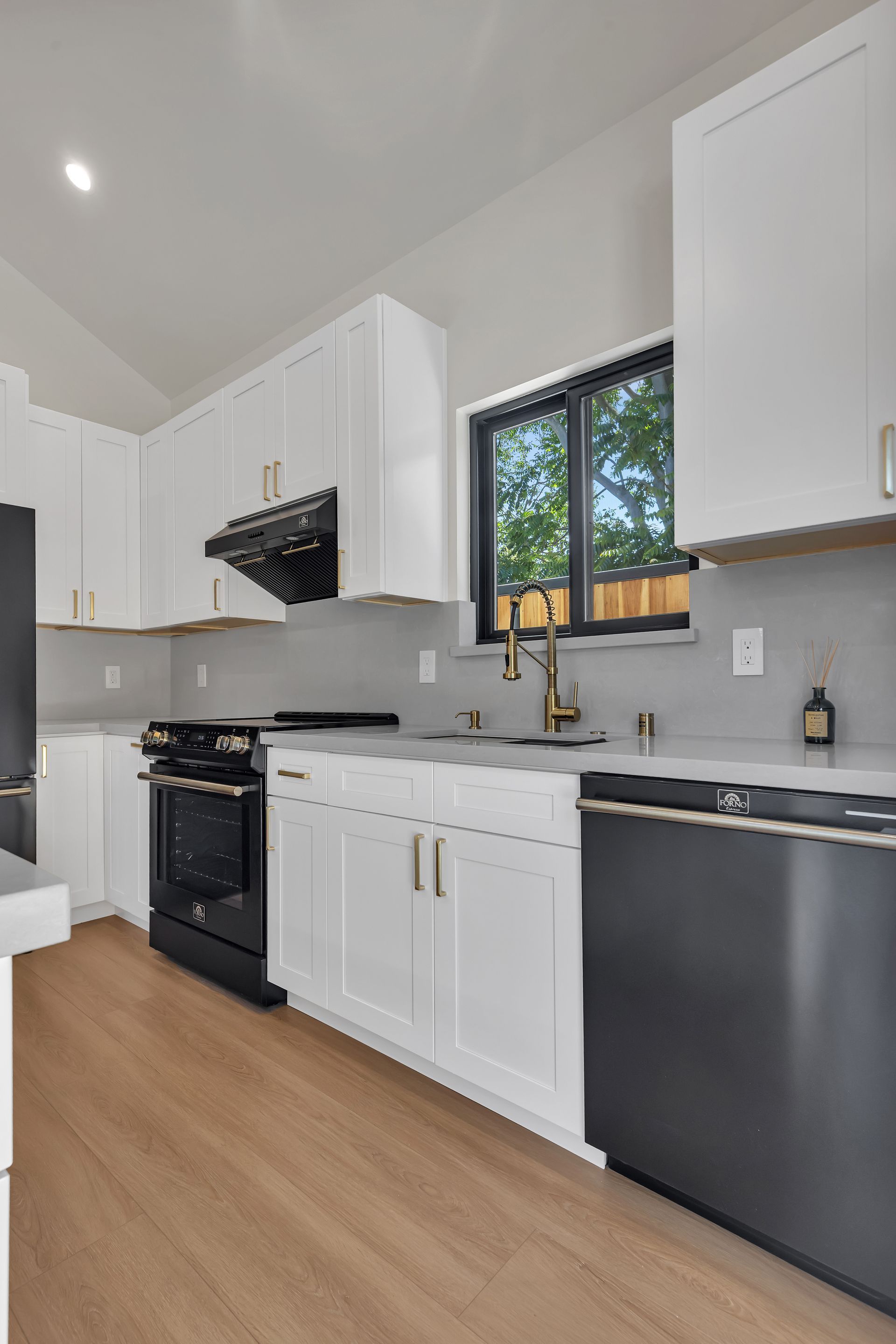 White kitchen with black appliances, gold hardware, and a window.