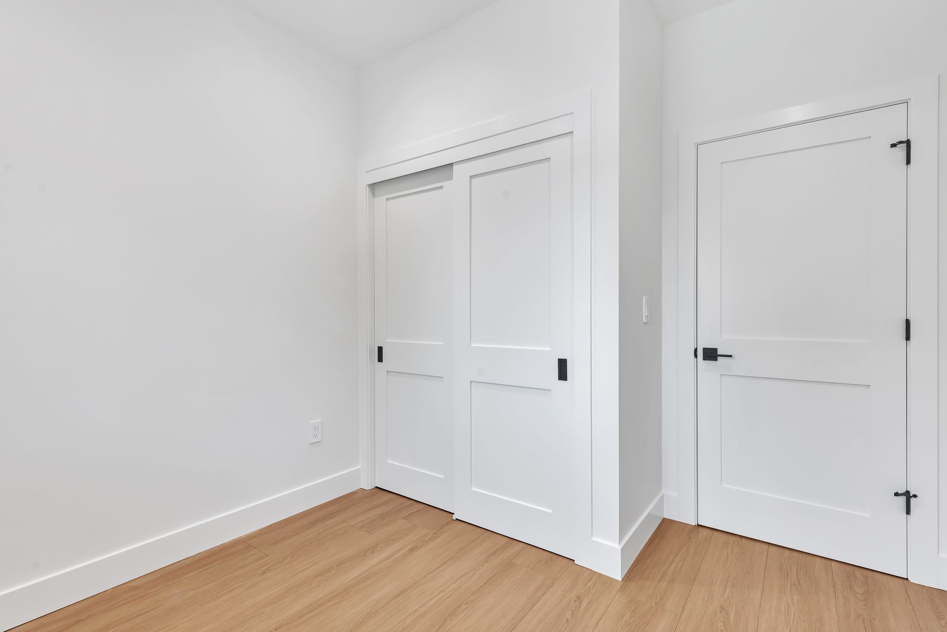 Empty, white room with light wood floors, a closet with sliding doors, and a closed door.