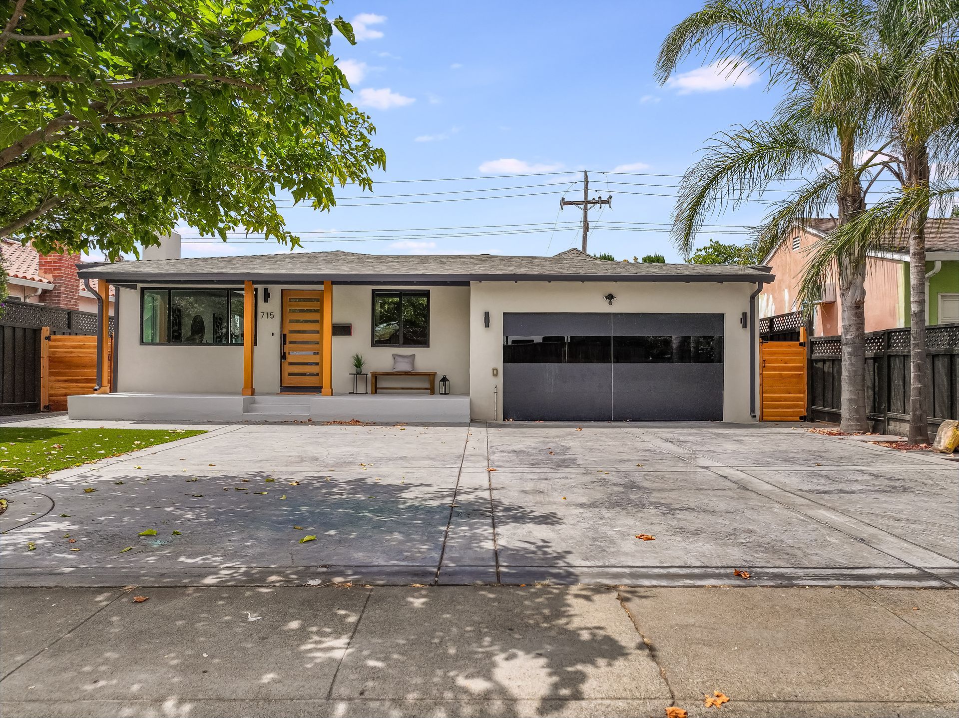 Single-story house with a gray garage door, yellow front door, and driveway under leafy trees.