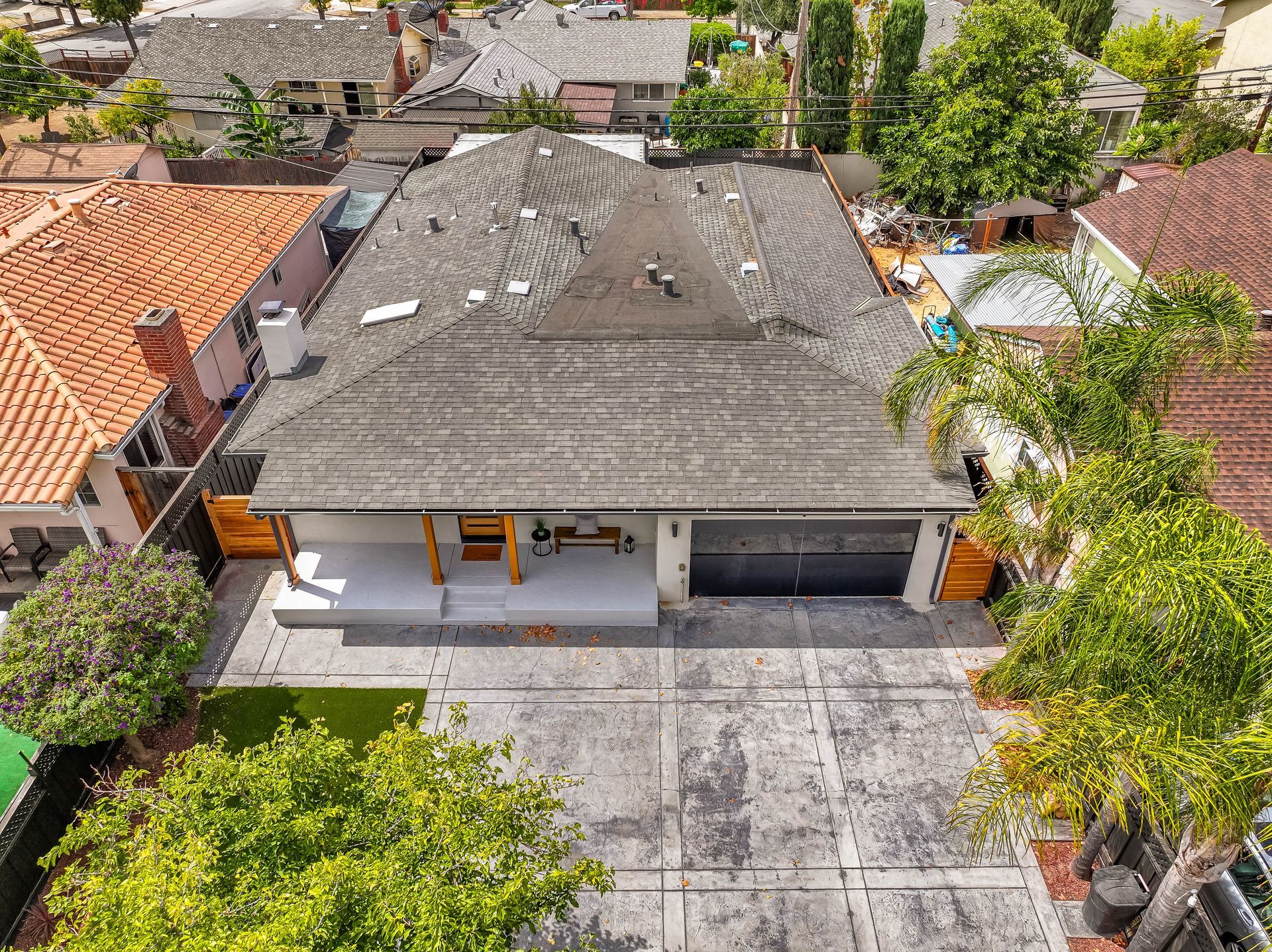 Aerial view of a single-story house with a gray roof, driveway, and trees in a residential neighborhood