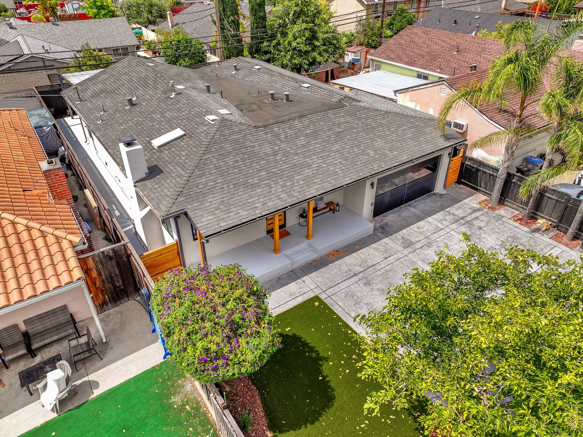 Aerial view of a gray-roofed house with a driveway and trees in a suburban neighborhood