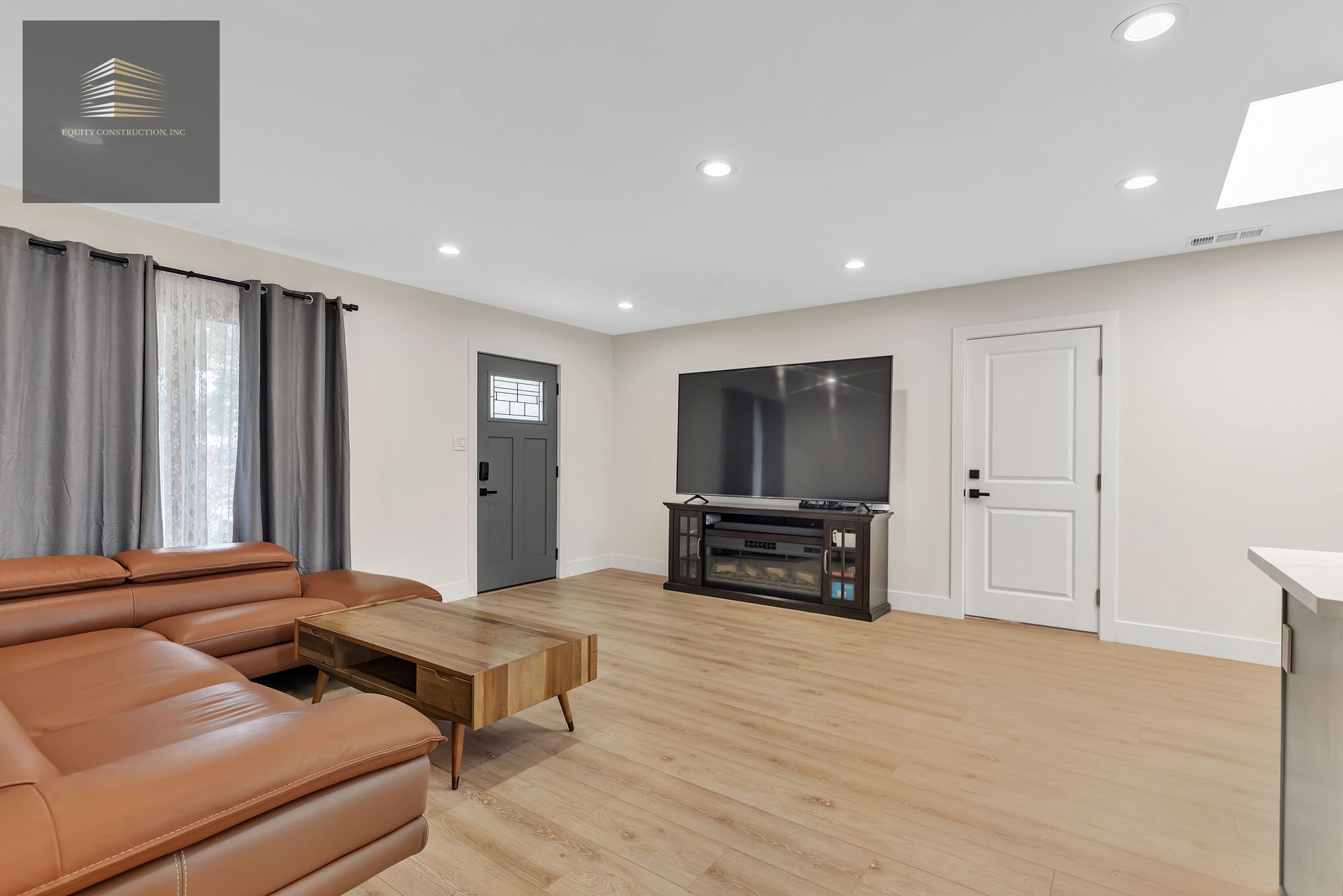 Living room with a brown leather sectional, large TV, wood floors, and a gray door.