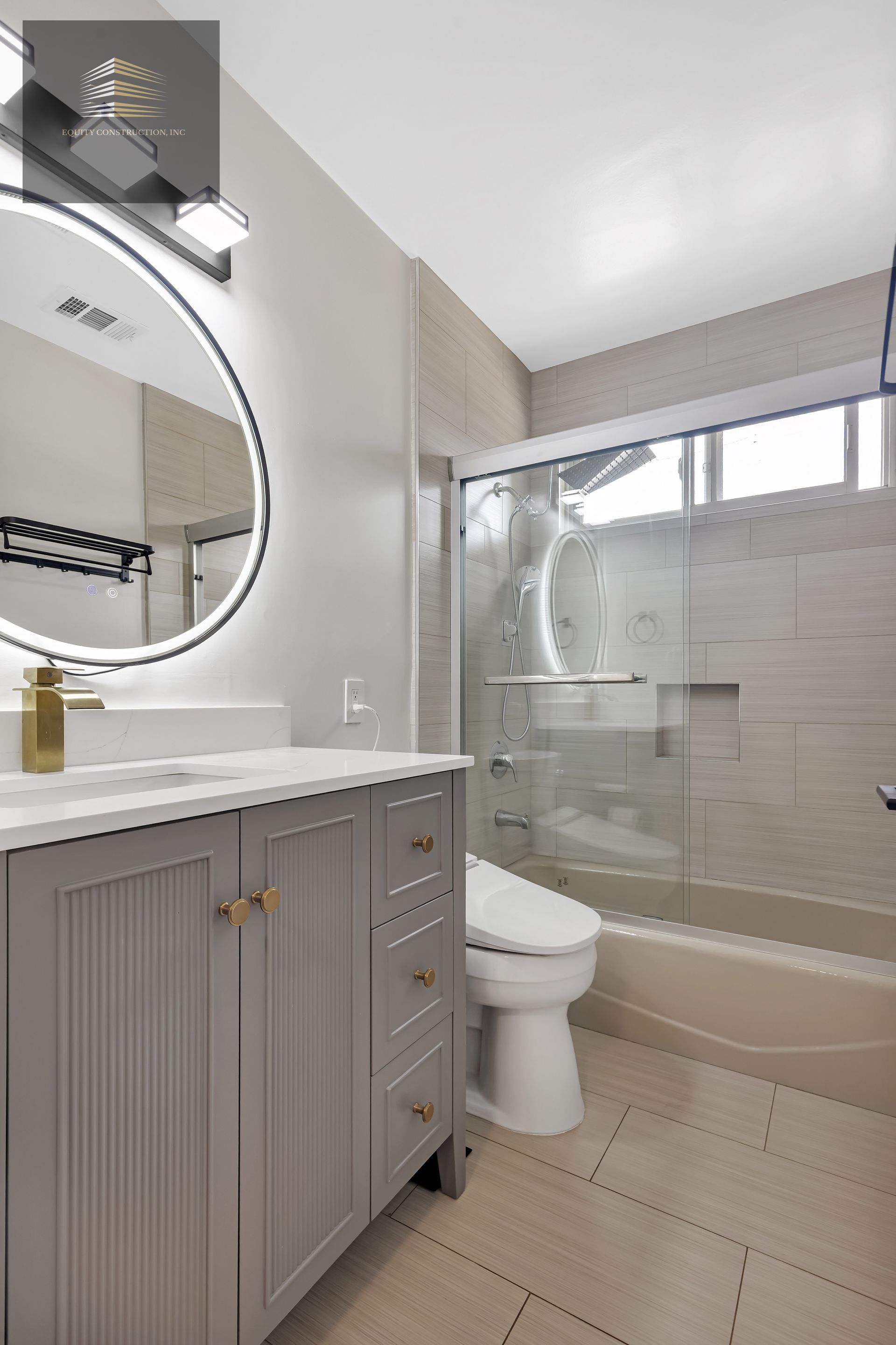 Bathroom with gray vanity, round mirror, glass shower door, and beige tile.