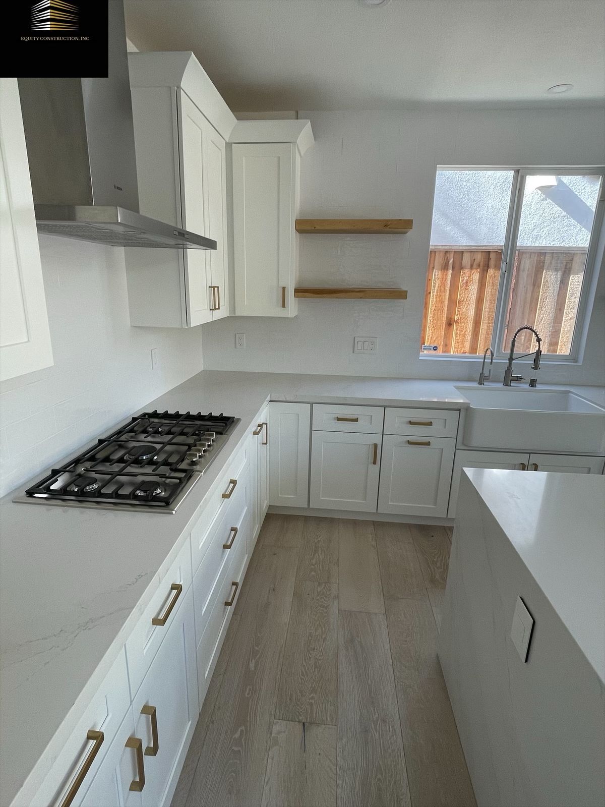 White kitchen with cabinets, countertops, and appliances. Includes a gas stovetop and floating shelves.