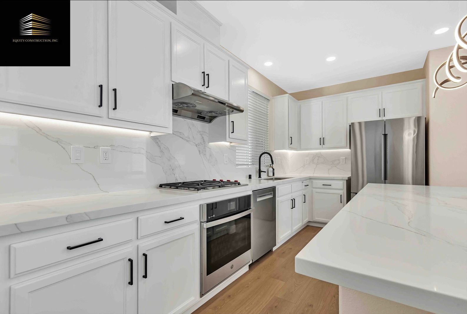 Modern white kitchen with stainless steel appliances, marble backsplash, and under-cabinet lighting.