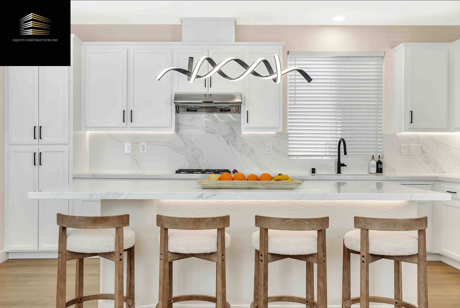 White kitchen with island, marble backsplash, modern light fixture, and wooden bar stools.