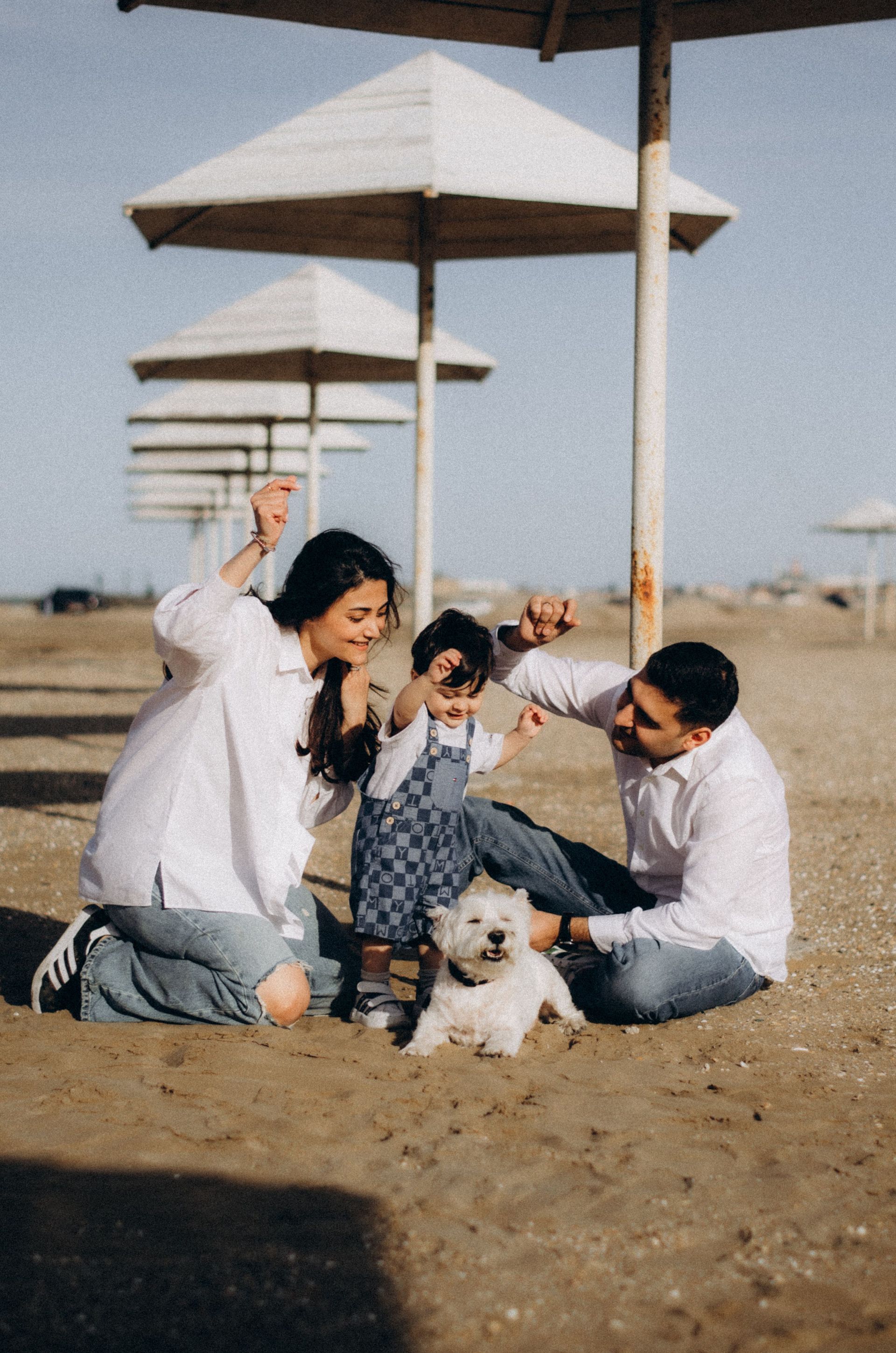 Family and small dog sitting on sandy ground under parasols outdoors
