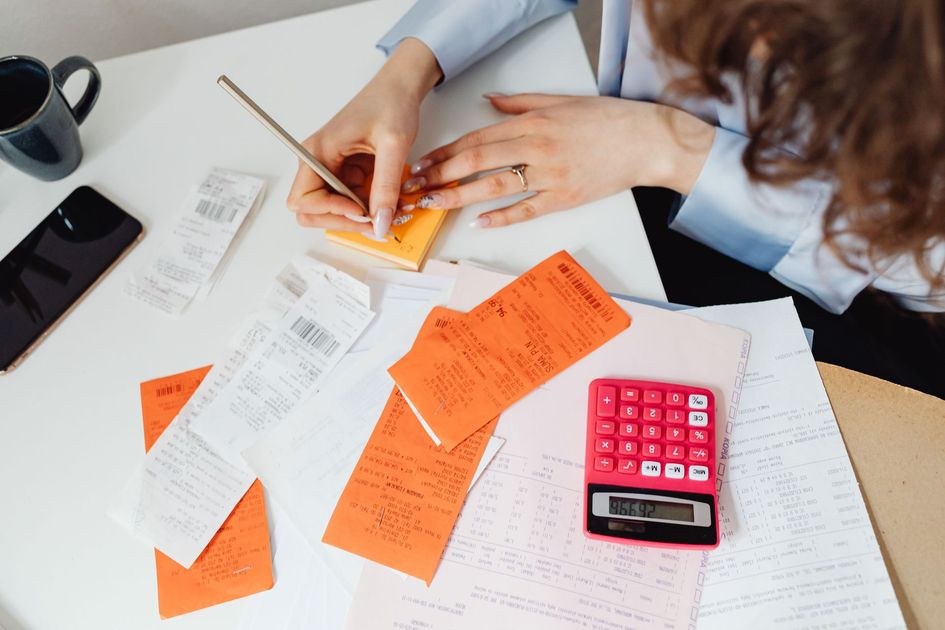Hands writing on orange notes at a desk with papers and a pink calculator
