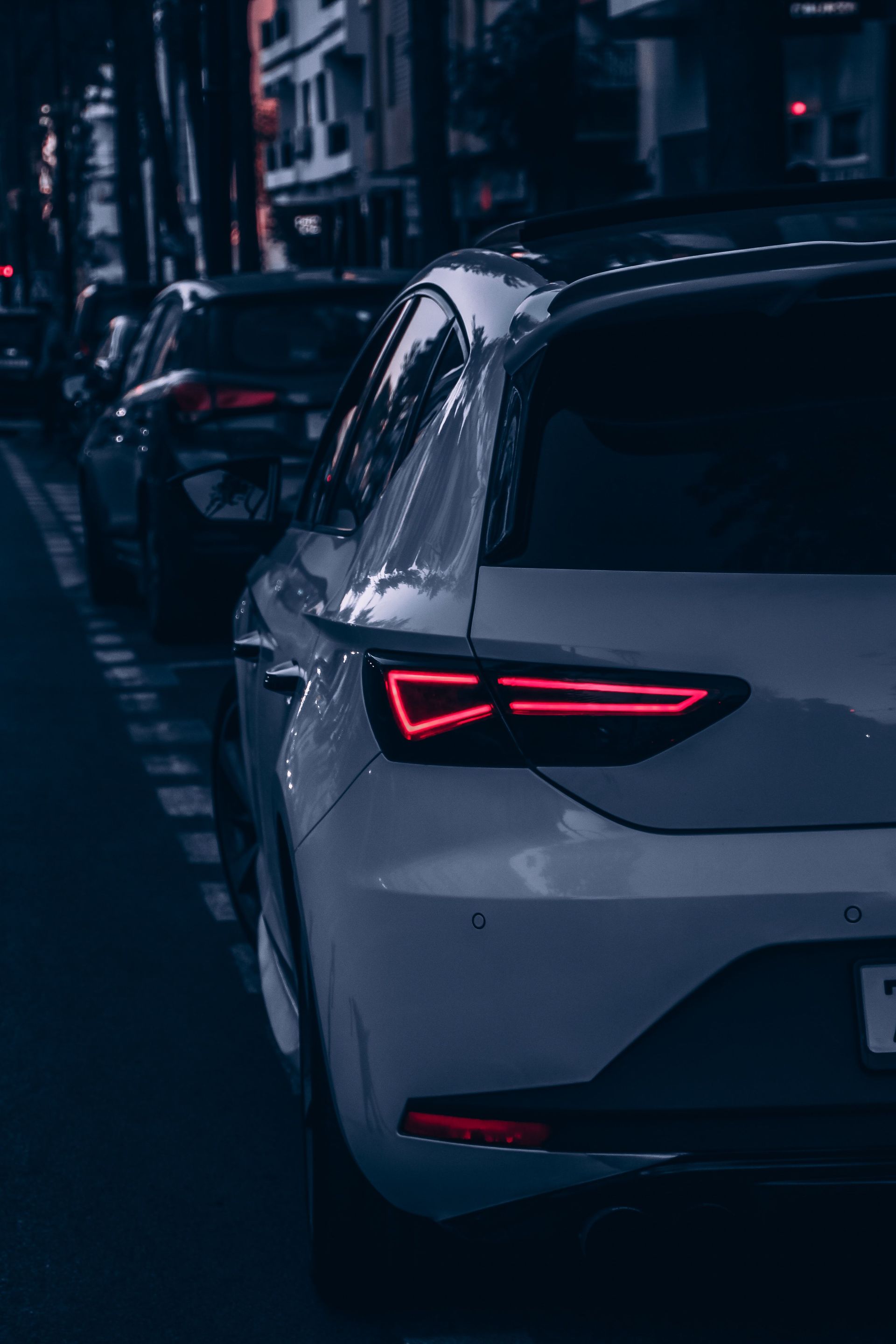 White SUV parked on a dark city street at night, viewed from the rear with red taillights glowing.