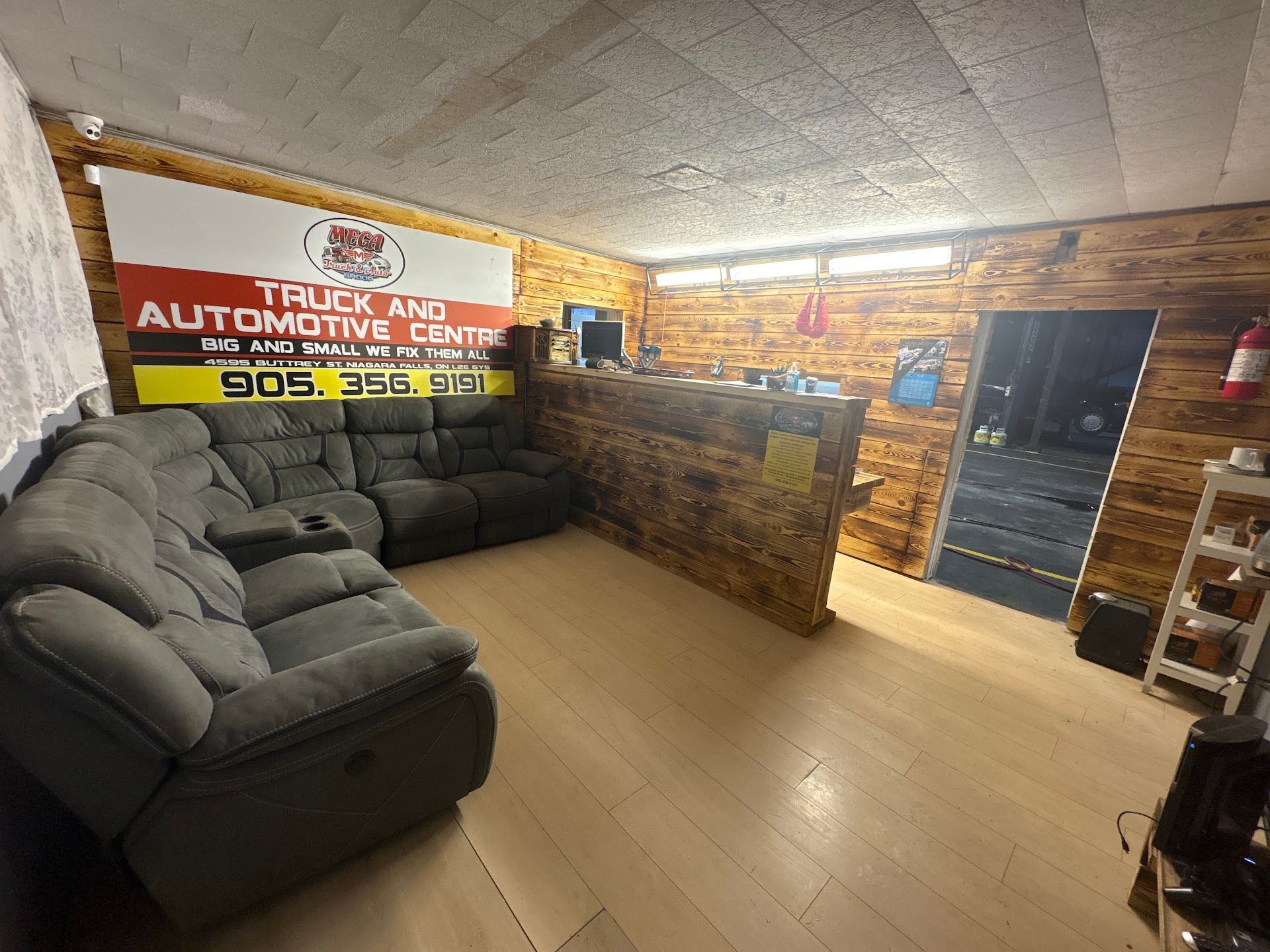 Interior of an automotive center waiting area with a recliner sofa, desk, and a sign.| Mega City Auto Niagara | Mega City Auto Niagara