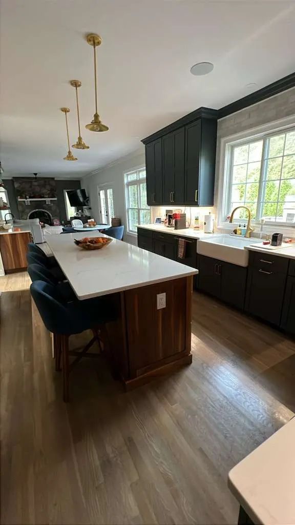 Modern kitchen with long island, dark cabinets, pendant lights, and large window over the sink