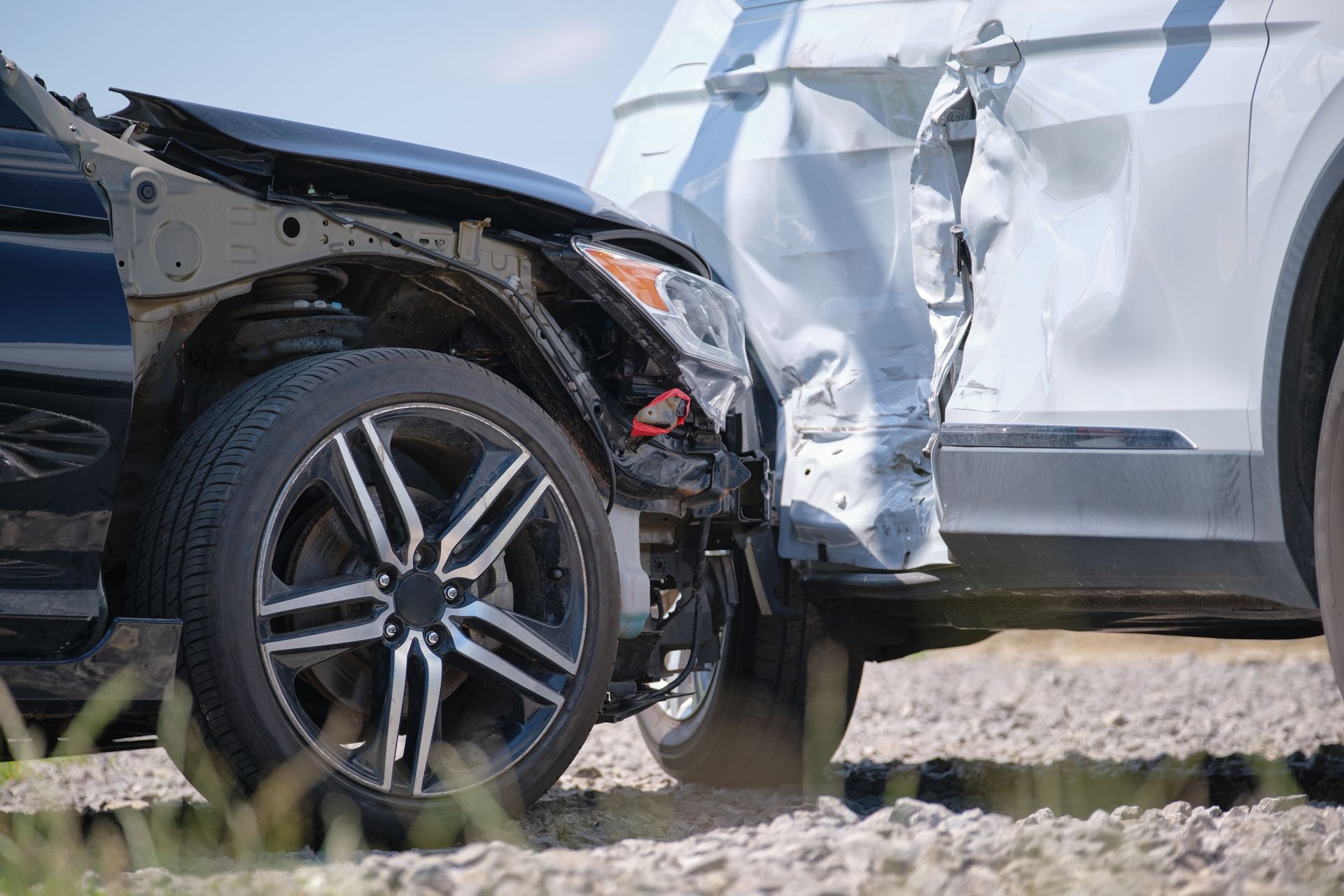 Two damaged cars, black and white, after a collision on a gravel surface.