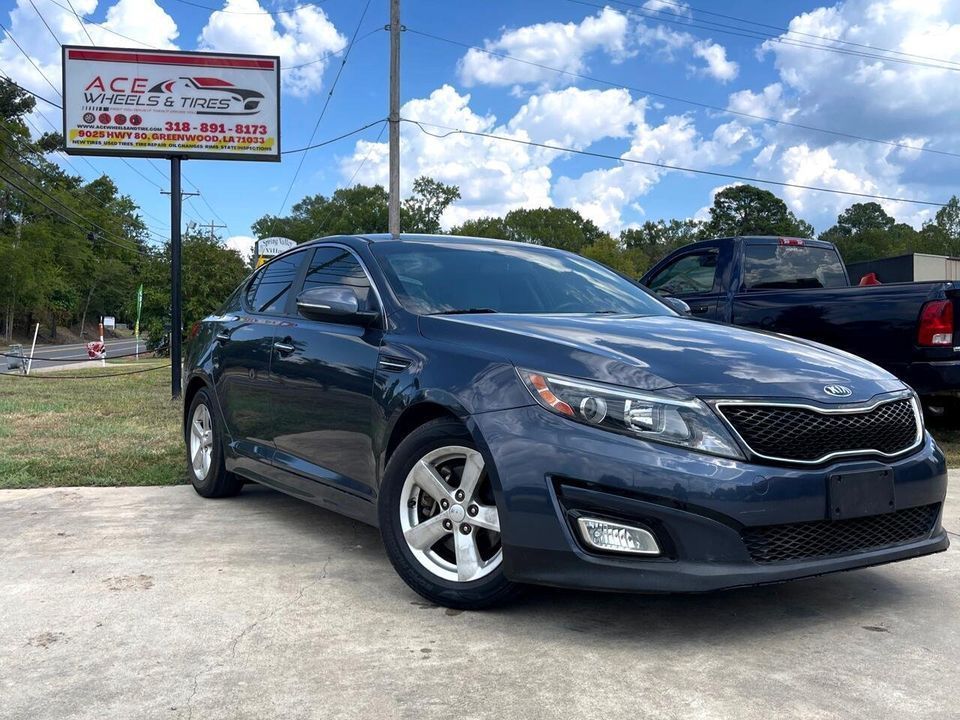 Dark blue Kia Optima parked in front of Ace Car Sales sign on a sunny day.