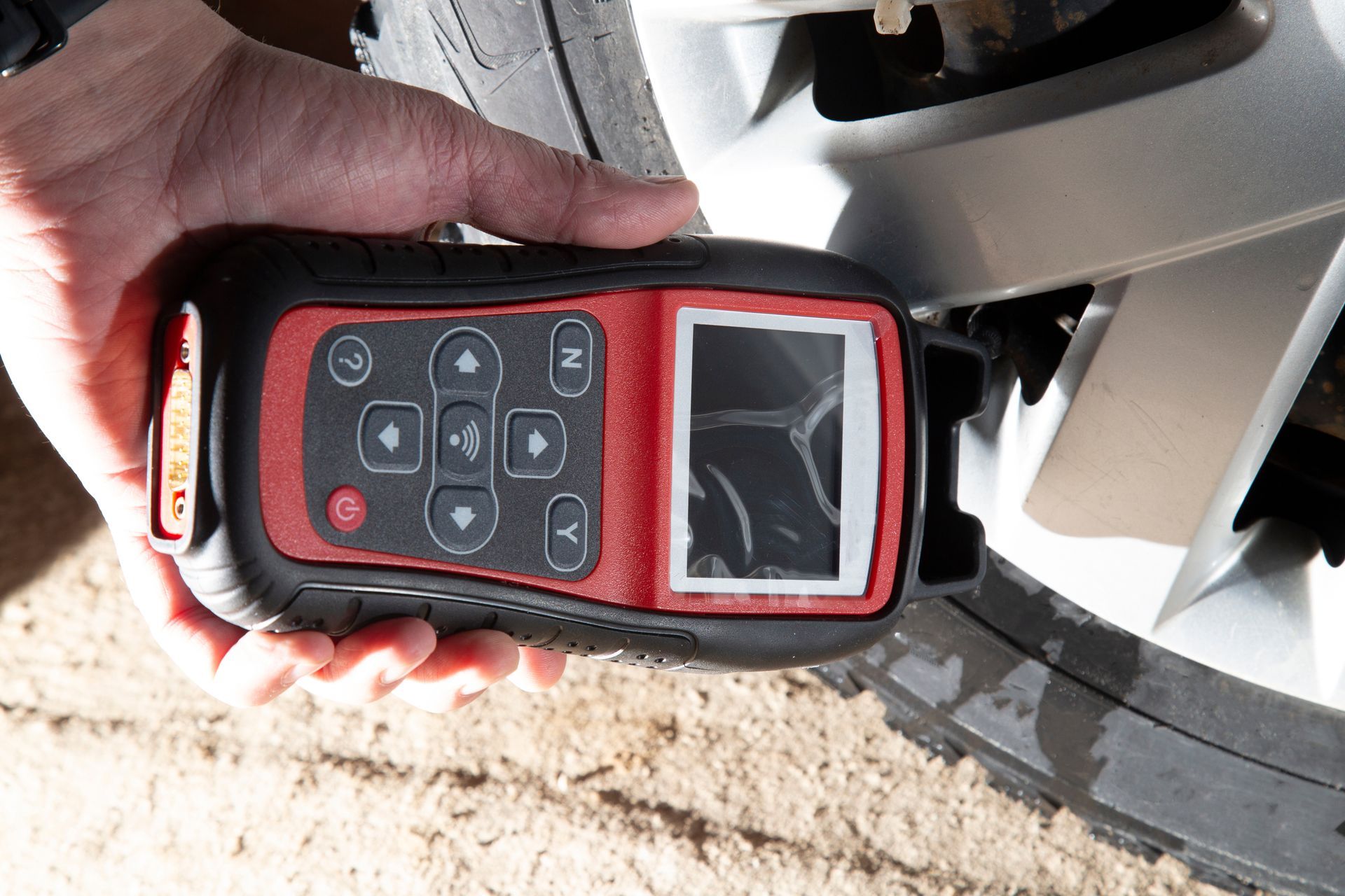 Hand holding a red and black TPMS tool near a car tire.