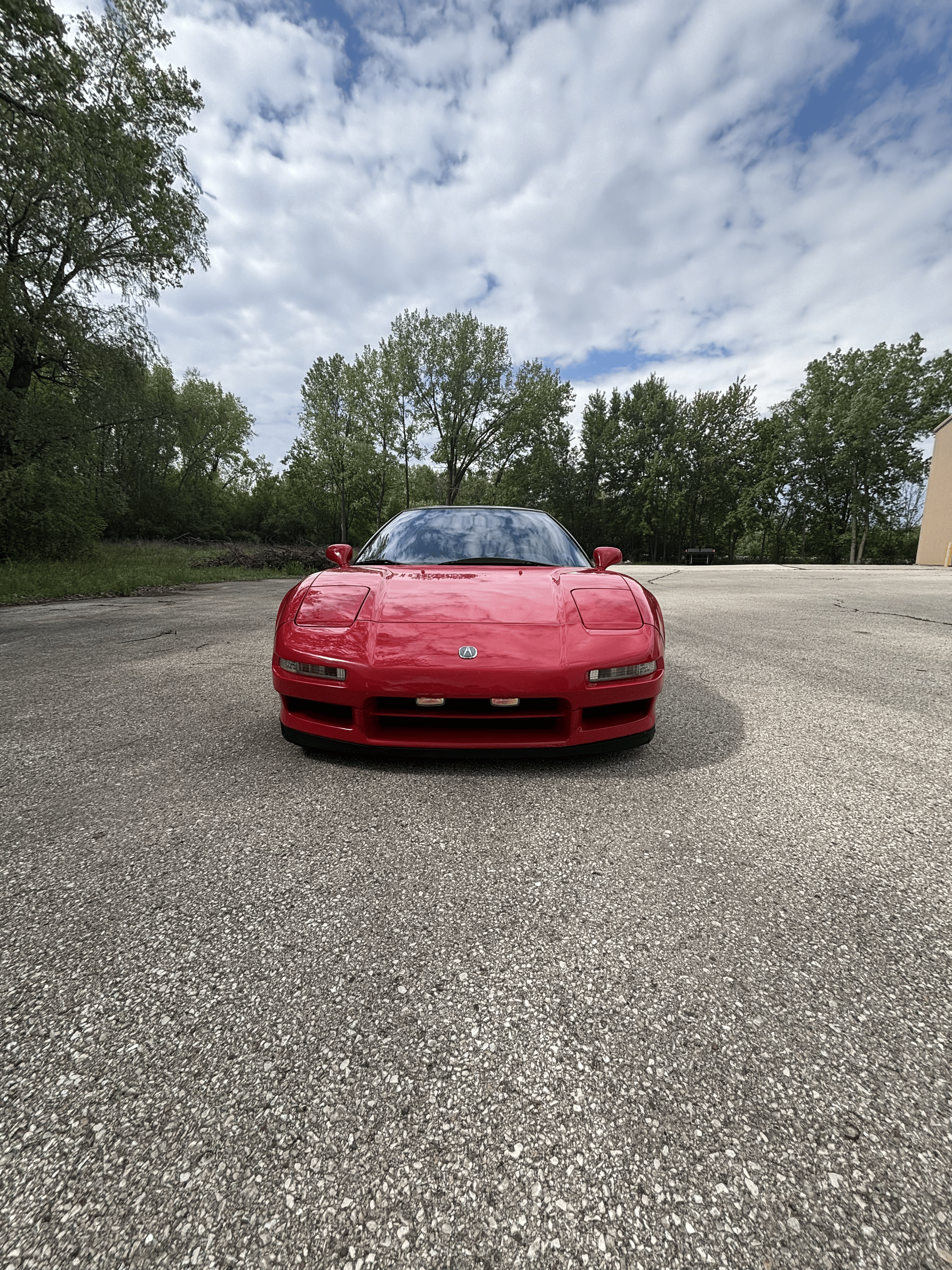 A red sports car is parked in a gravel lot.