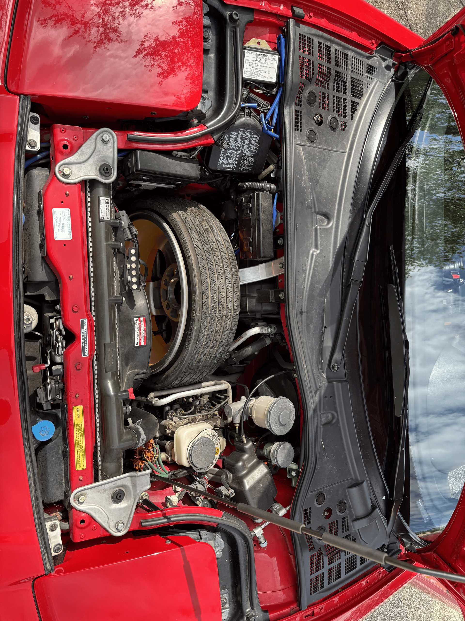 The engine of a red car is shown with the hood open.