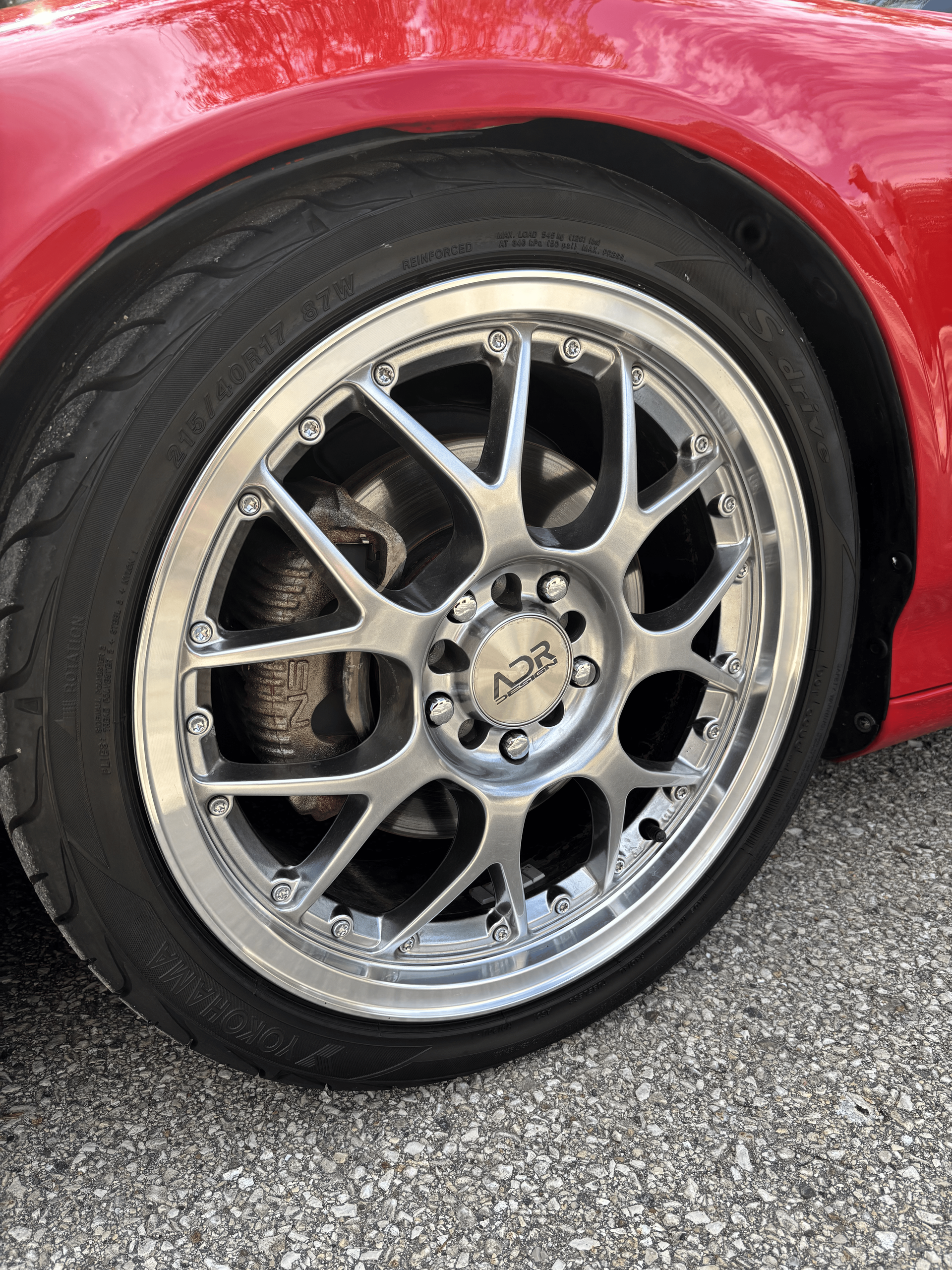 A close up of a red car wheel on a gravel road.