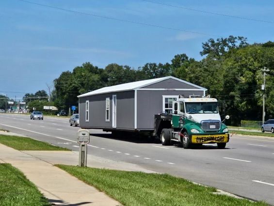 A truck is carrying a building down a street.
