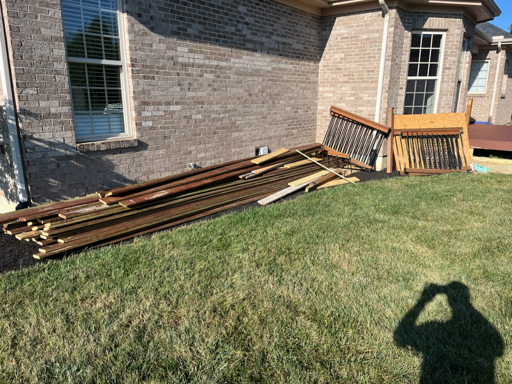 A pile of wood is sitting in the grass in front of a brick house.