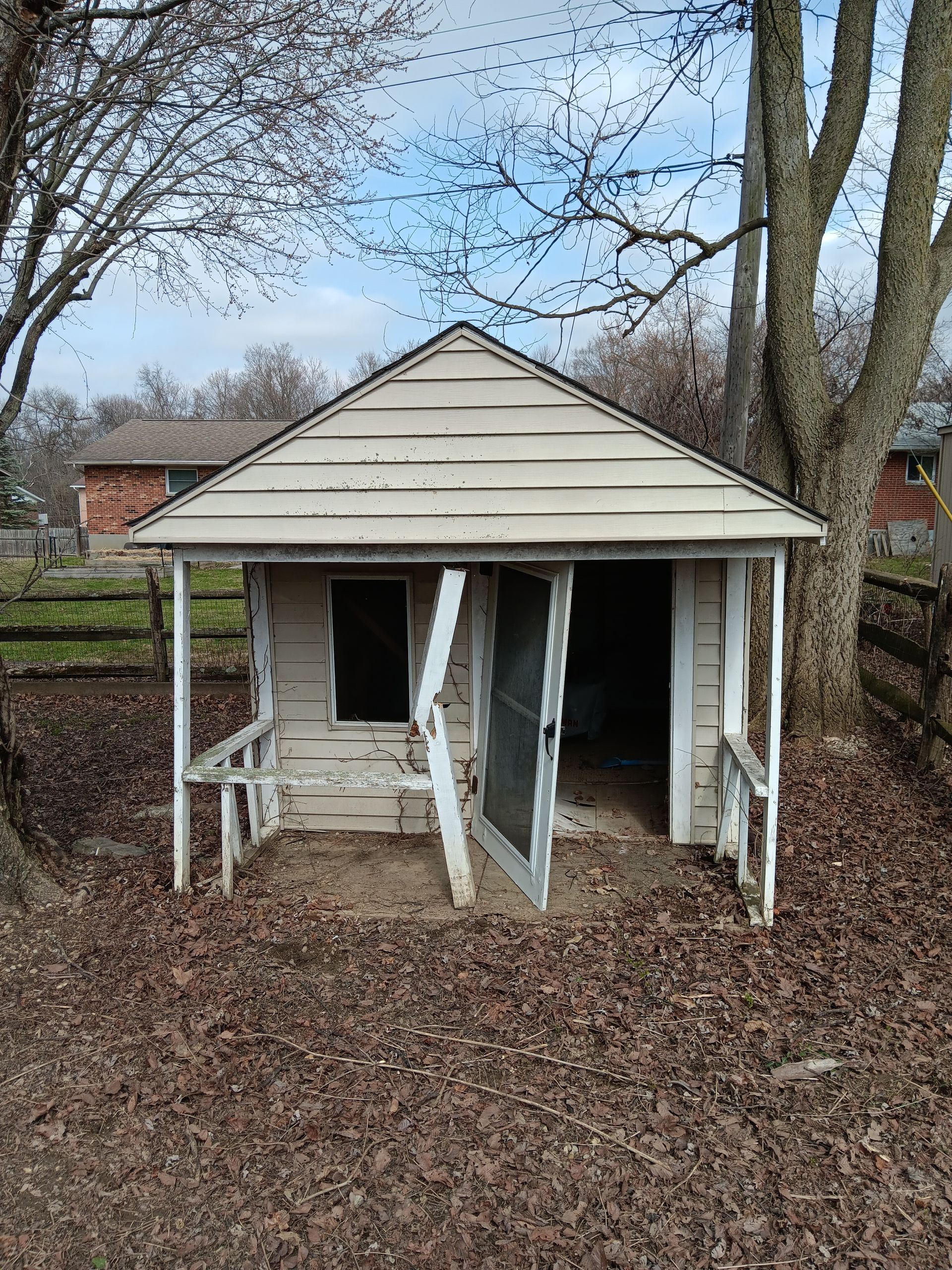 A small white house with a porch is surrounded by trees and leaves.