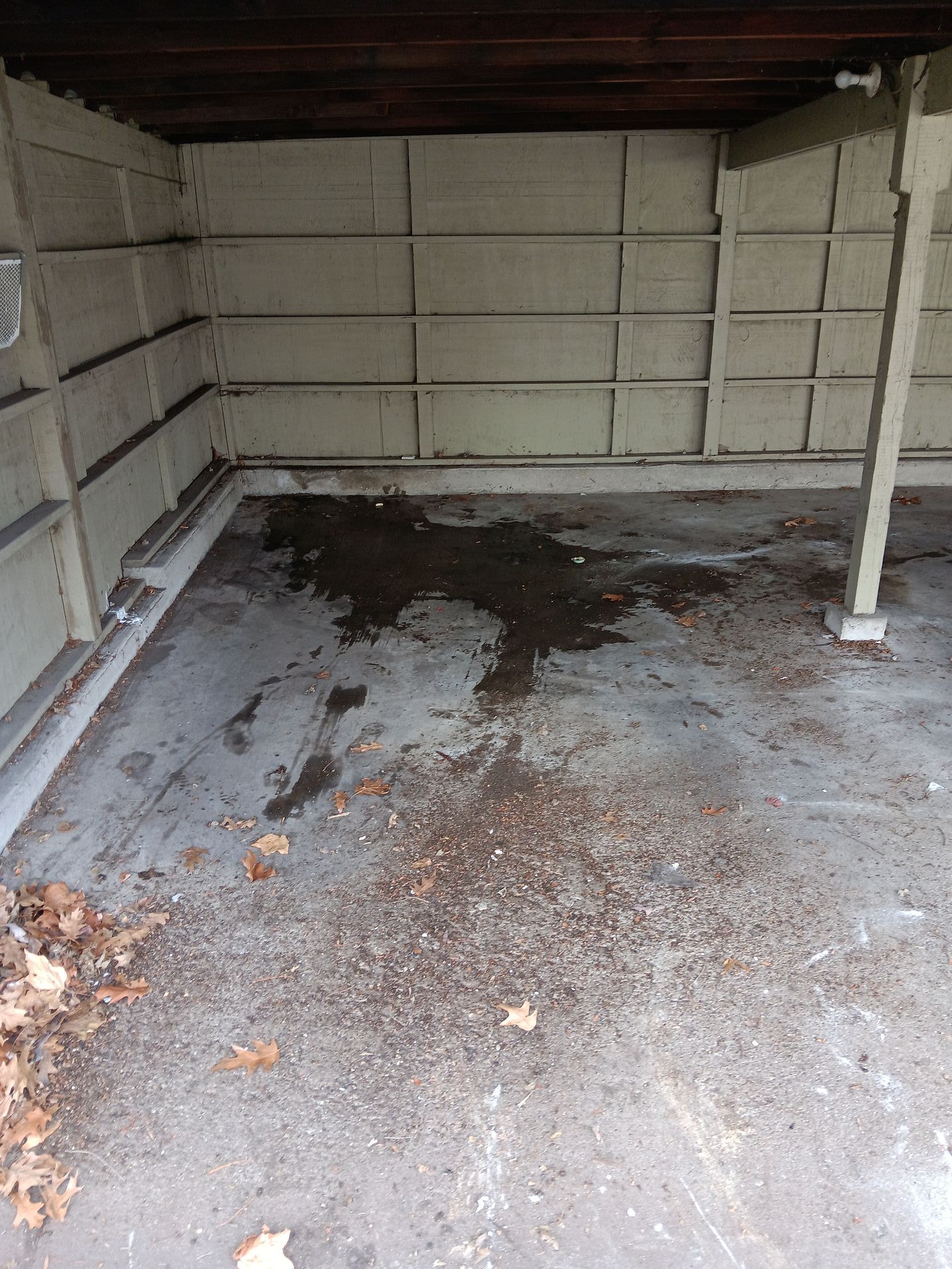 A dirty garage with a lot of leaves on the floor.