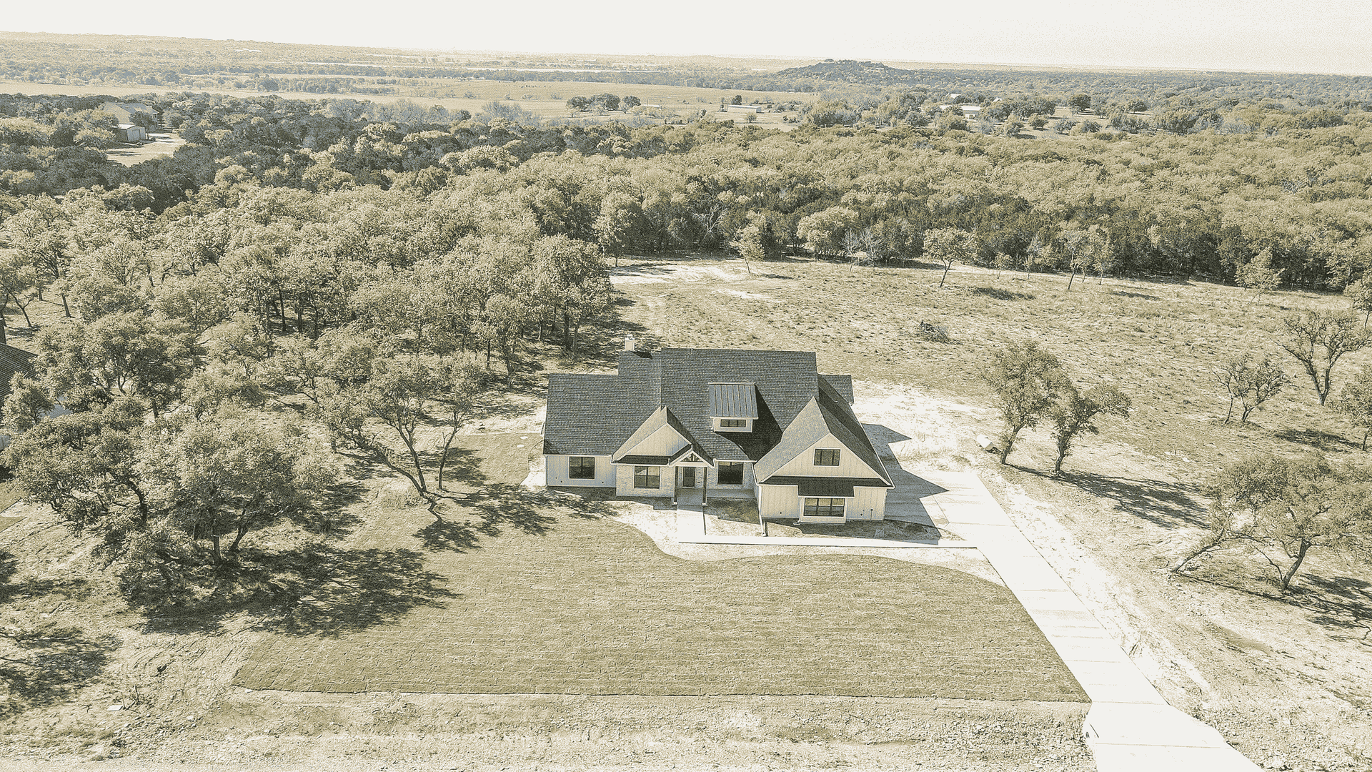 An aerial view of a house in the middle of a field surrounded by trees.