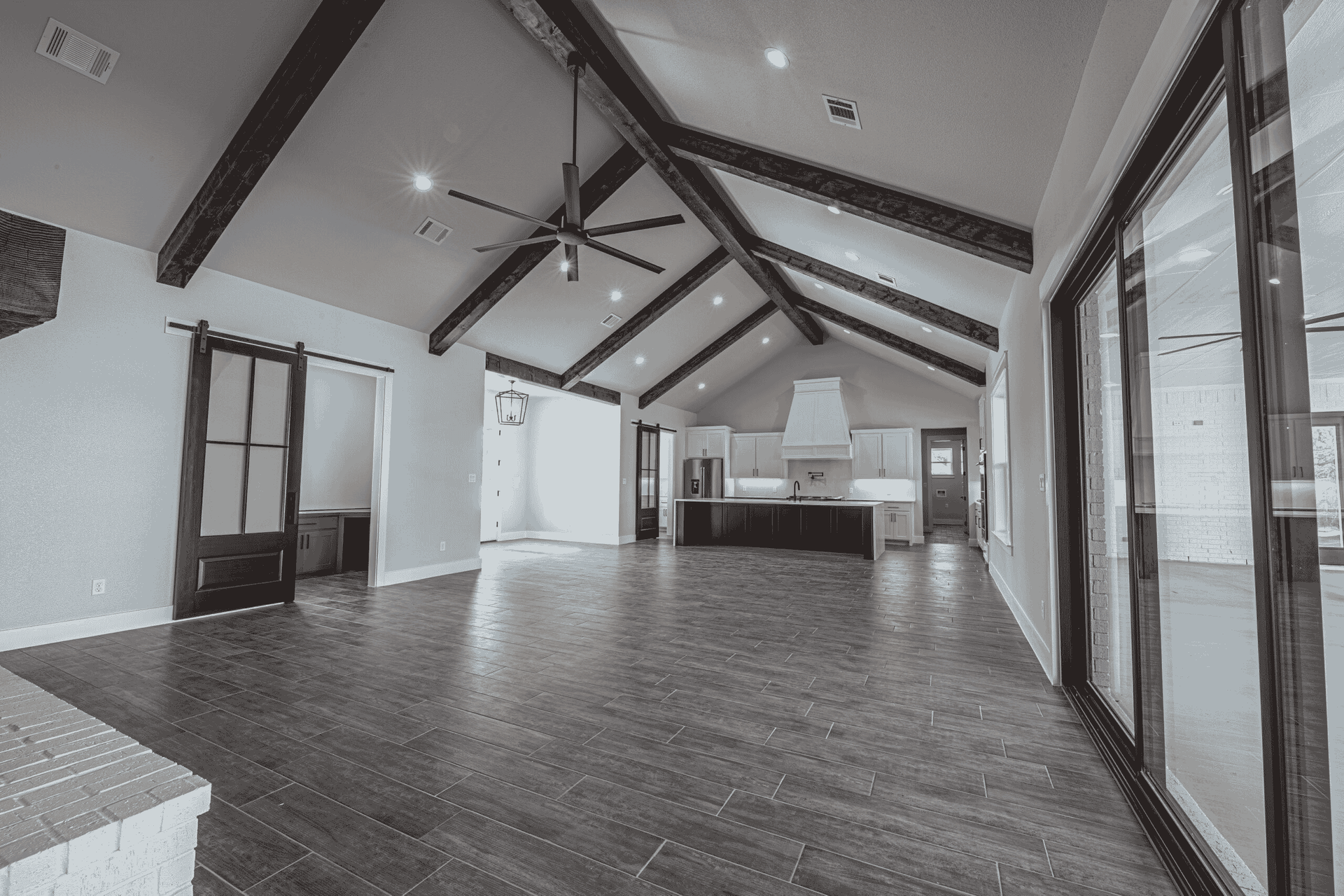 A black and white photo of an empty house with hardwood floors and a vaulted ceiling.