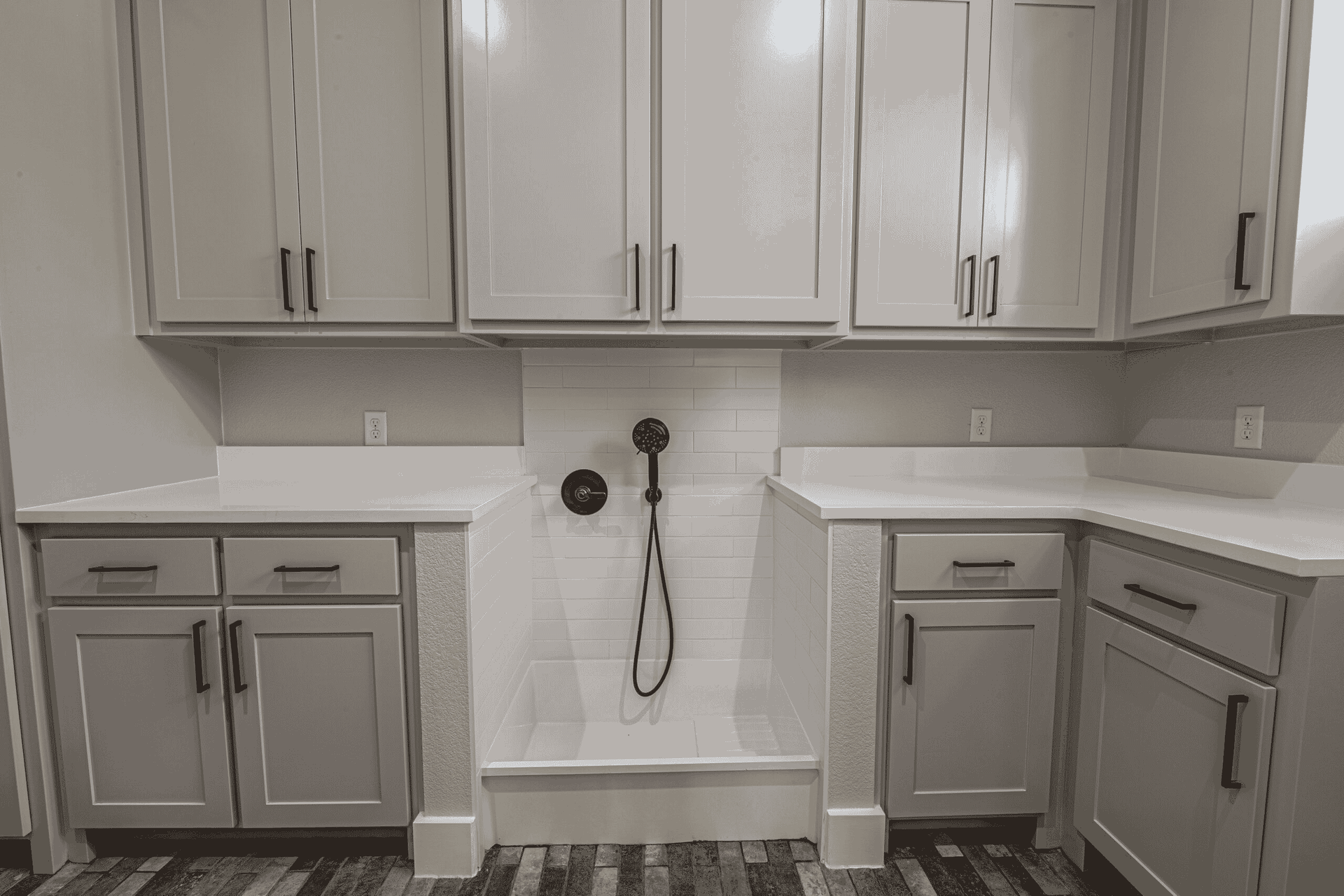 A black and white photo of a laundry room with white cabinets and a dog shower.