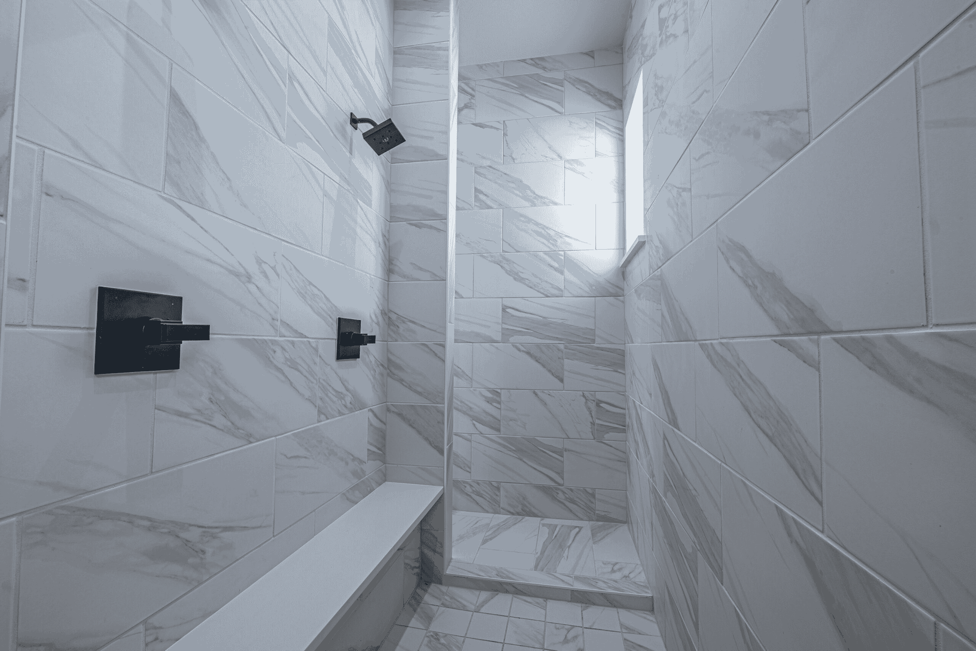A bathroom with marble tiles and a walk in shower with a bench.